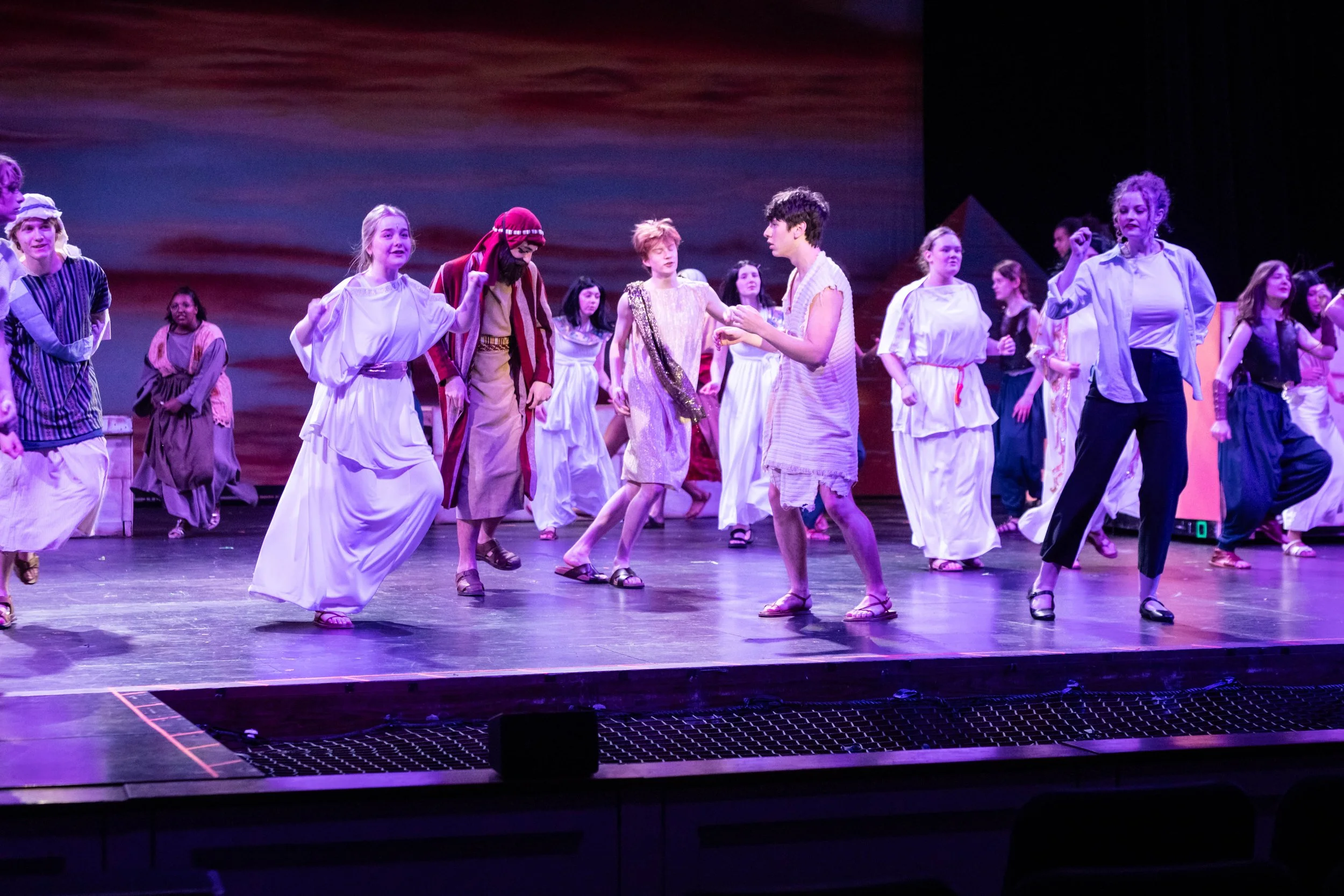 Theater performance on stage with actors dressed in costumes resembling ancient or biblical attire, engaging in dialogue or dance.