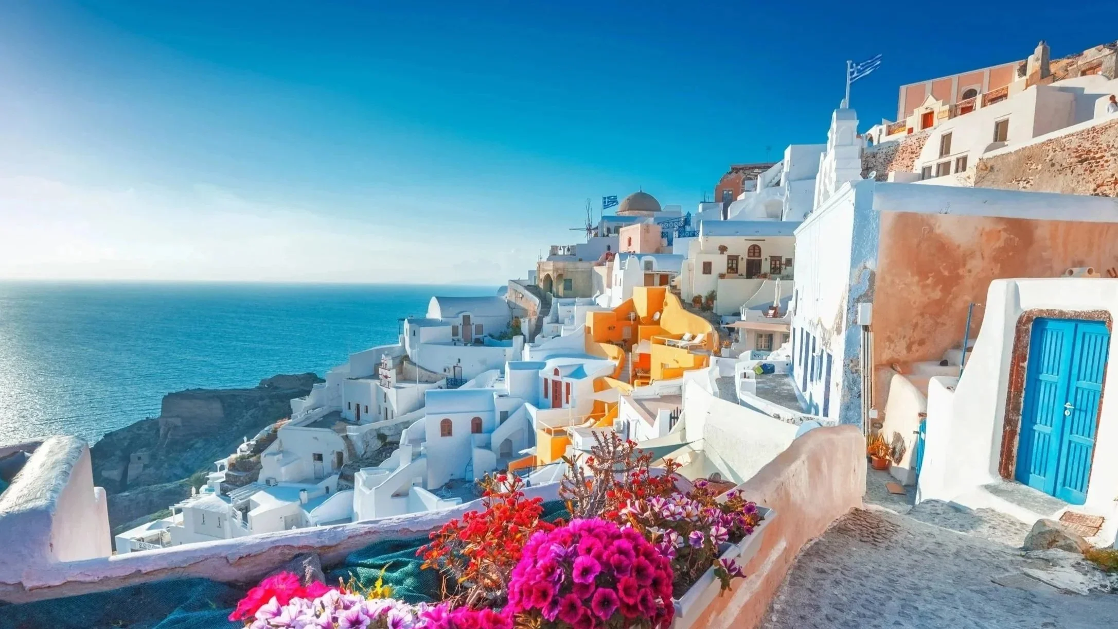 White buildings with colorful accents on a cliffside overlooking a blue sea in Santorini, Greece.