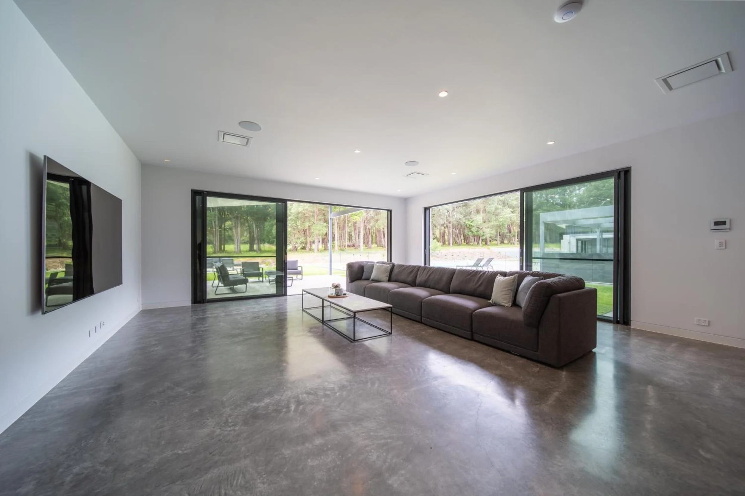 Another of Launa's living rooms with large windows, brown sofa, rectangular coffee table, and outside greenery