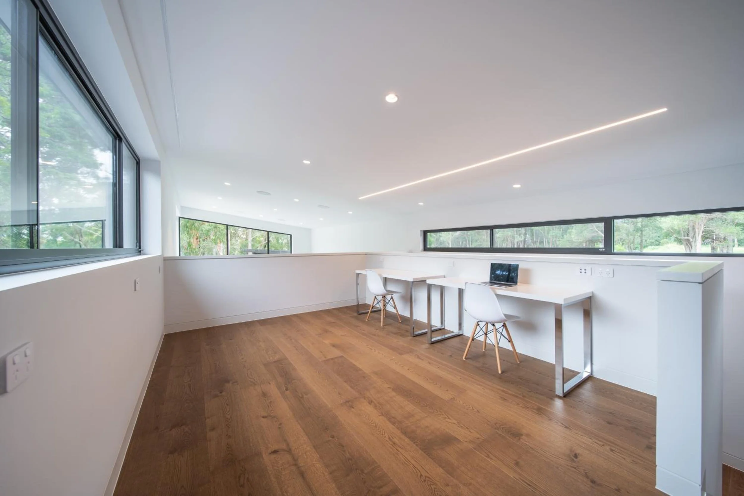 Launa's modern loft office space with large windows, white walls, a wooden floor, and a minimalist white desk with two white chairs. The windows overlook a green outdoor area.