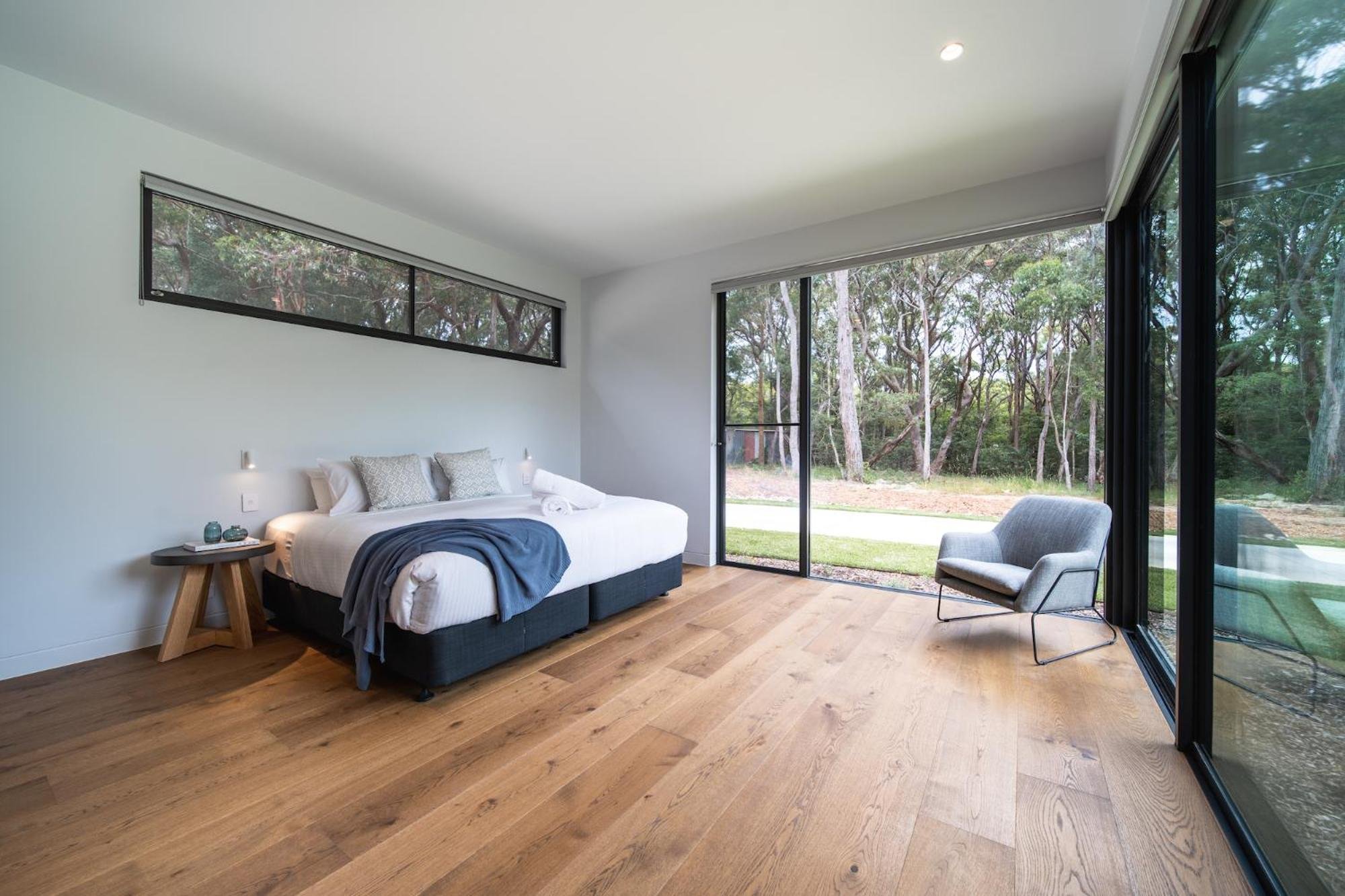 Another of Launa's bedrooms with a large sliding glass door showing a wooded backyard. The floor is made of light hardwood, and the ceiling has small recessed lighting.