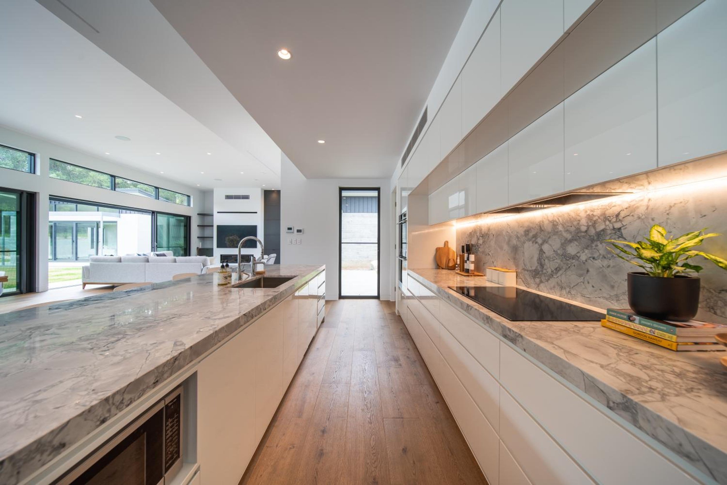 Launa's modern kitchen with marble countertops, white cabinets, and a view into living area with large windows and sliding door.