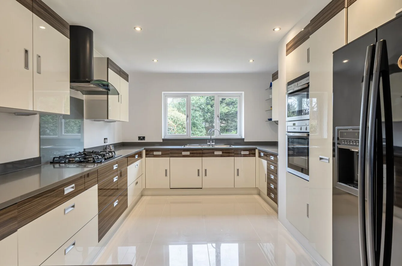 Modern kitchen with white cabinets, gray countertops, and a window overlooking greenery. Contains a built-in oven, microwave, refrigerator, and a gas stove.