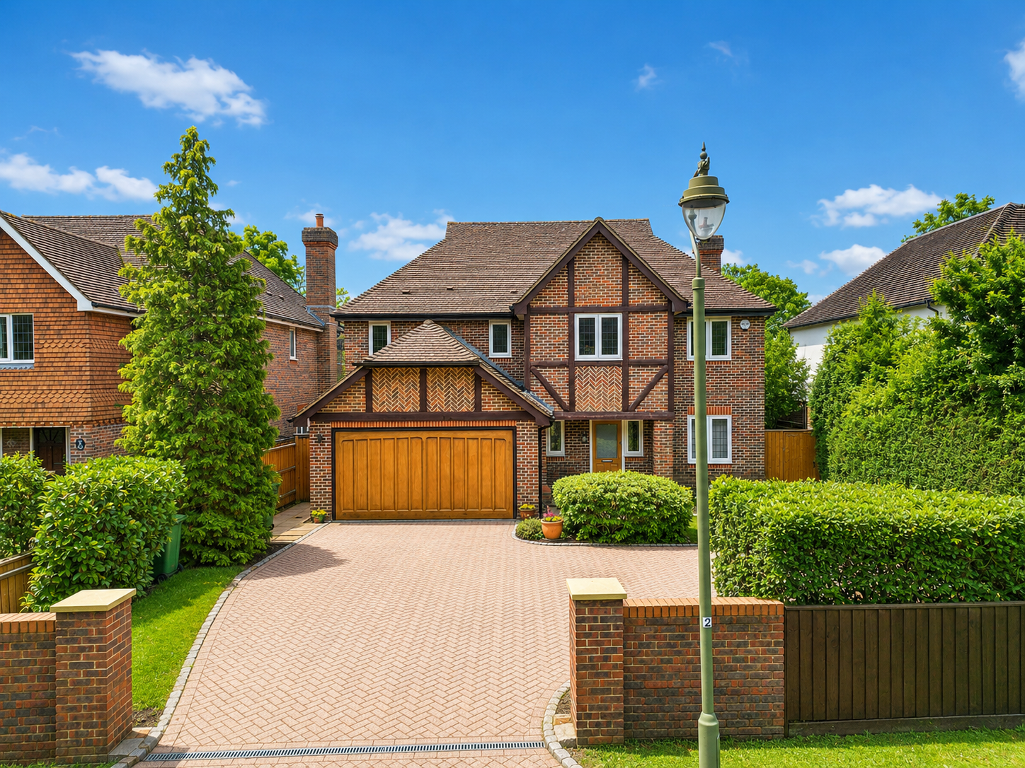 A large brick house with a wooden garage door, surrounded by trees and bushes, under a bright blue sky with a few clouds.