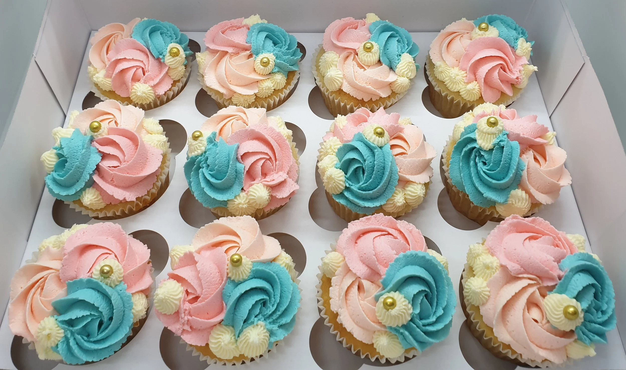 Box of 1 dozen cupcakes decorated with pink and blue swirled frosting and small pearl decorations.