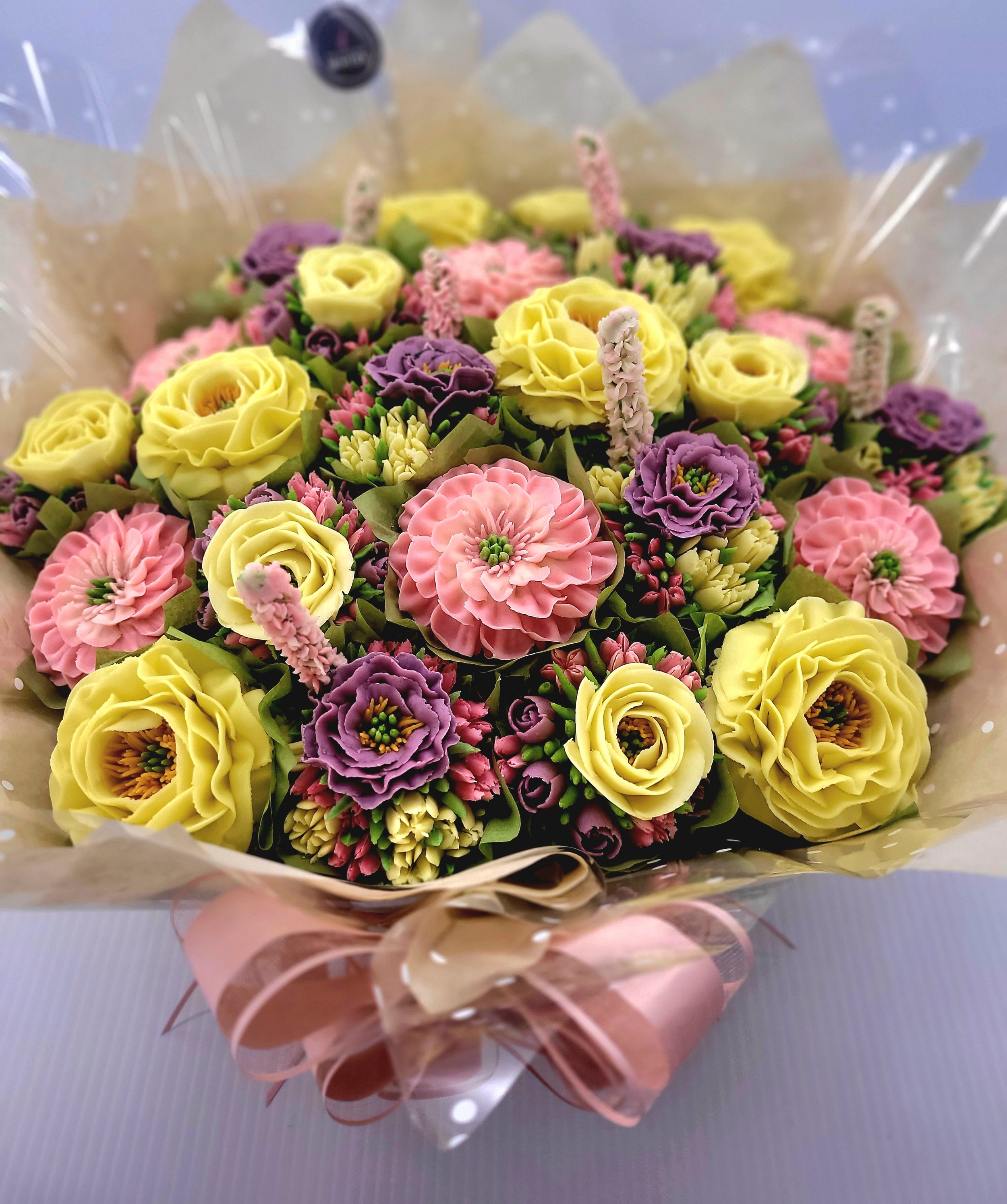 A vibrant floral buttercream cupcake bouquet of yellow, pinks and purple.