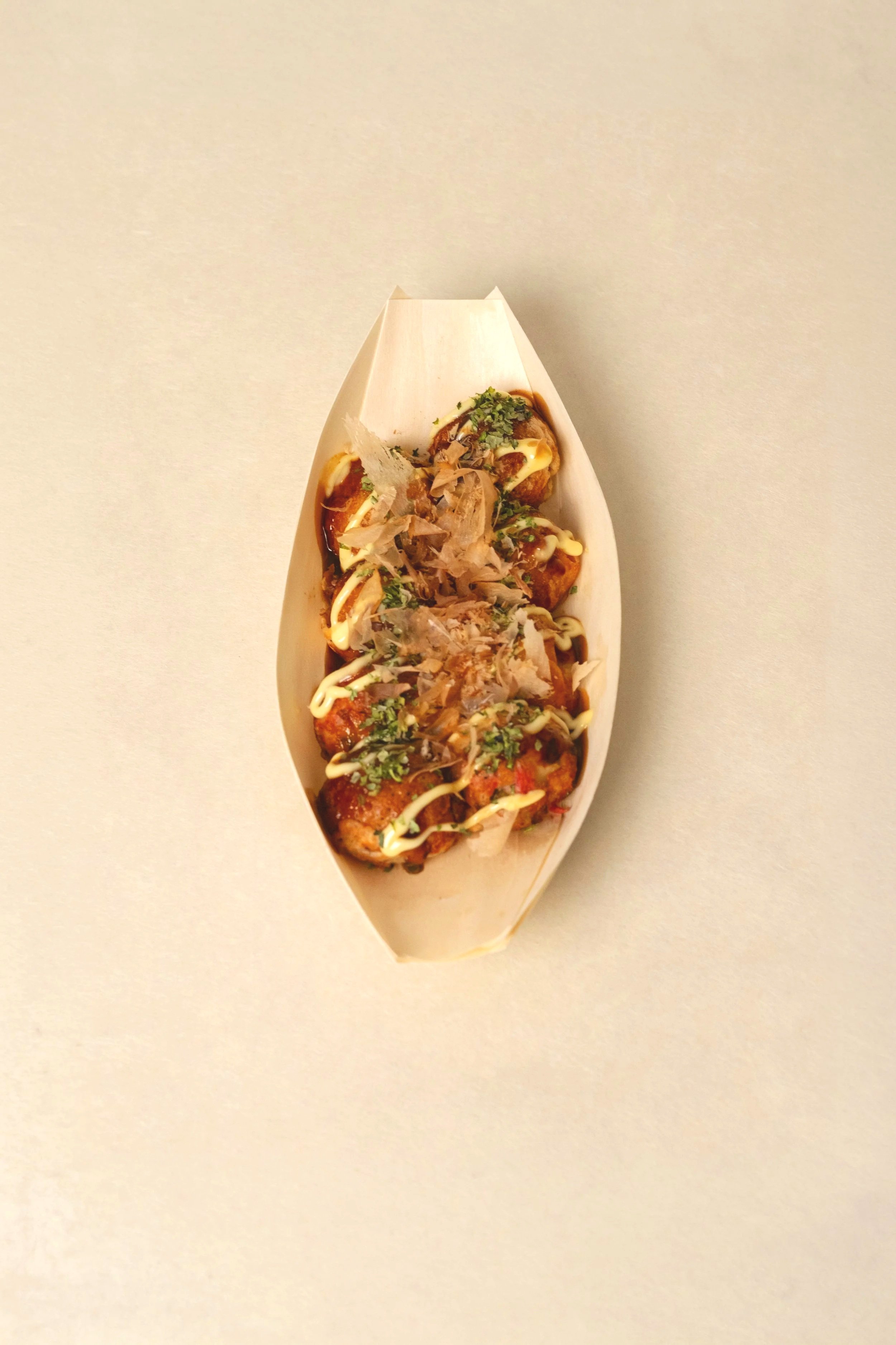 A boat-shaped container holding Japanese takoyaki topped with sauce, mayonnaise, green herbs, and bonito flakes. The classic.