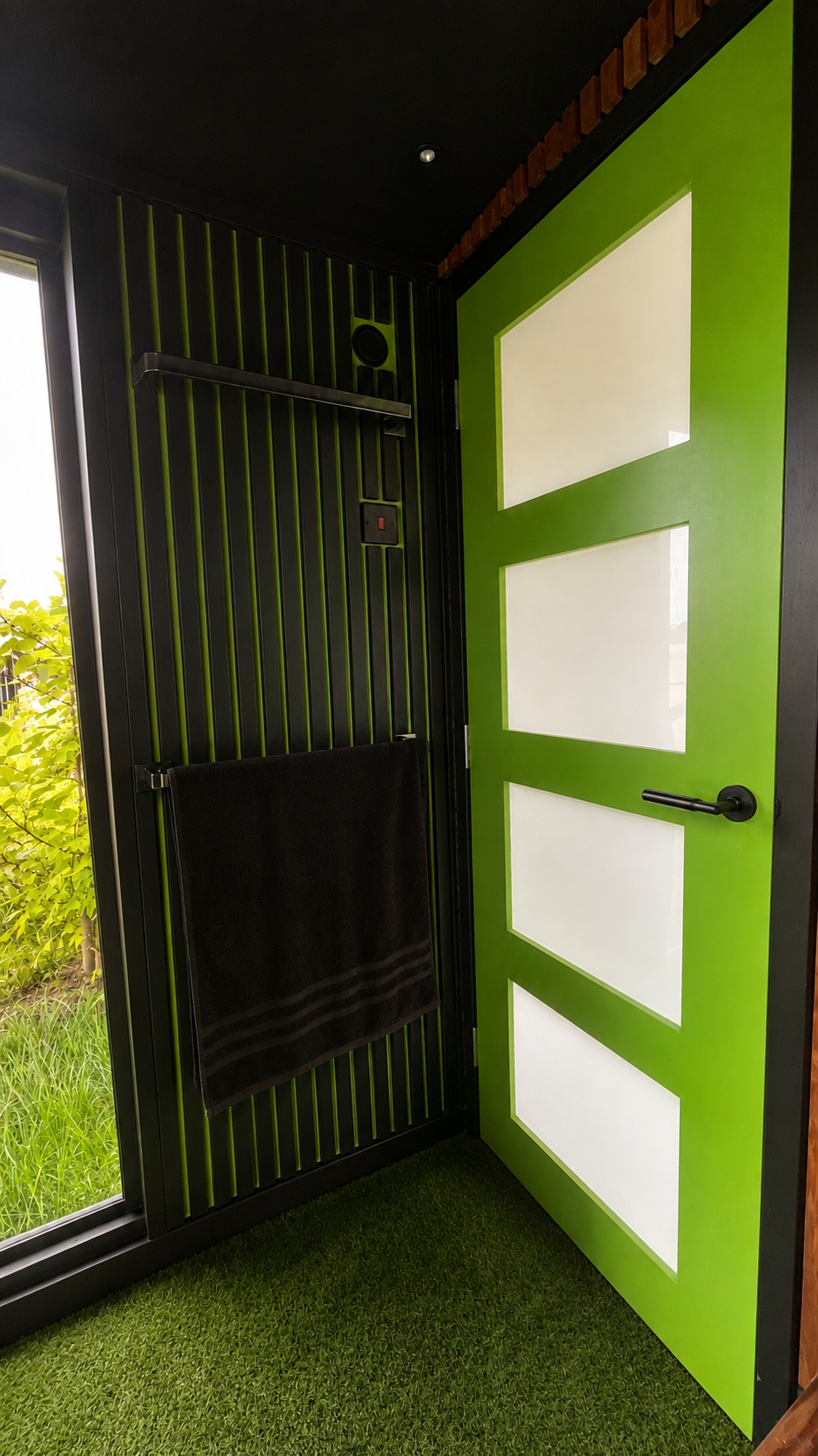 Black towel rail beside the green entrance door inside the PLUVIA enclosed outdoor shower room