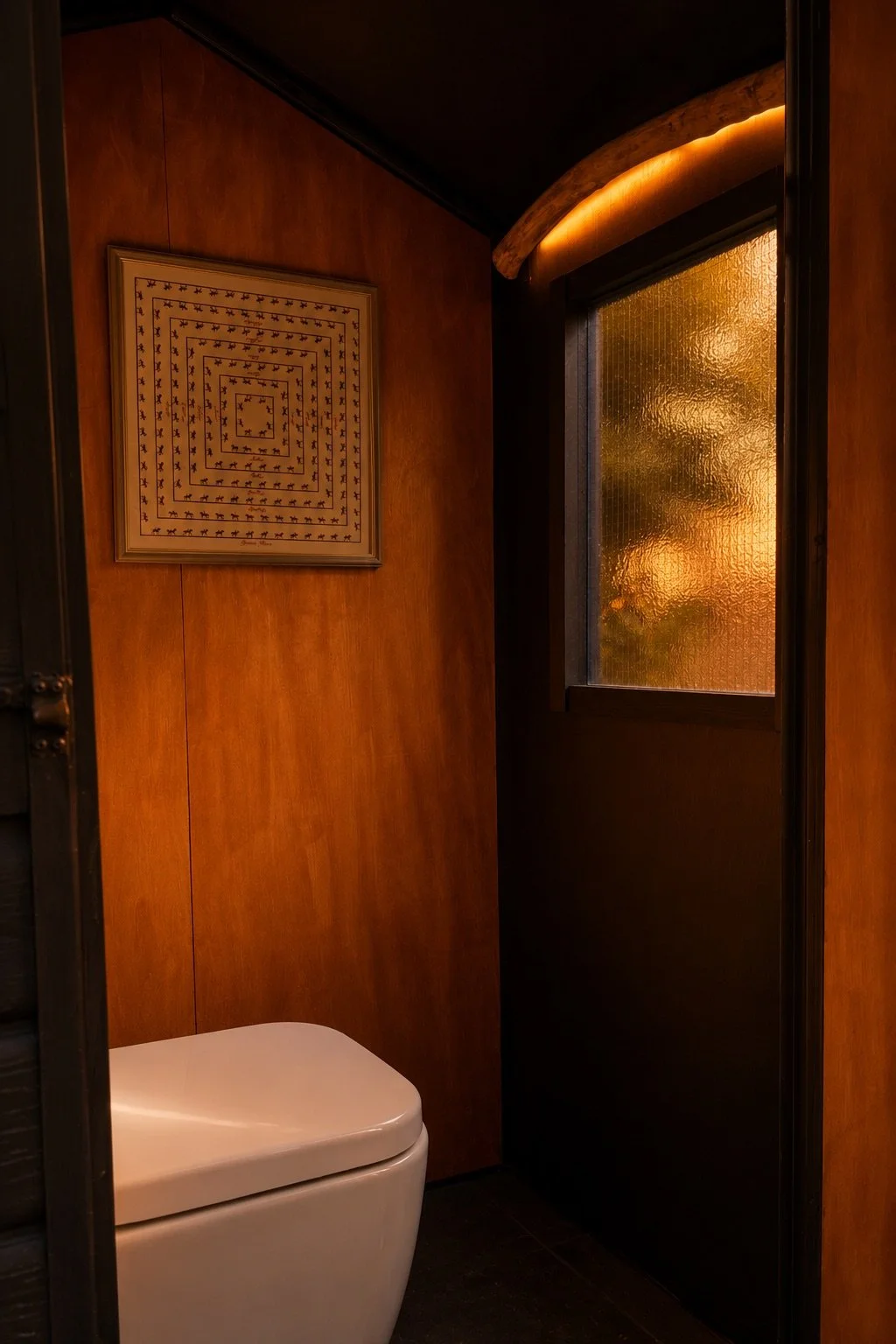 Timber-lined outhouse interior with a frosted window, sculptural illuminated timber detail and modern white toilet.