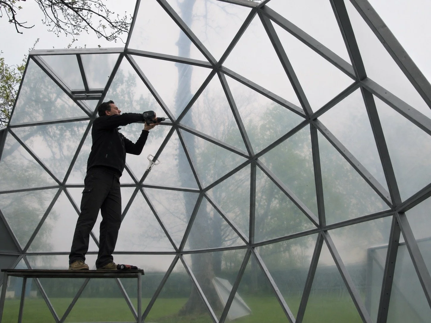 Designer assembling the triangular frame and transparent panels inside a geodesic dome during construction.