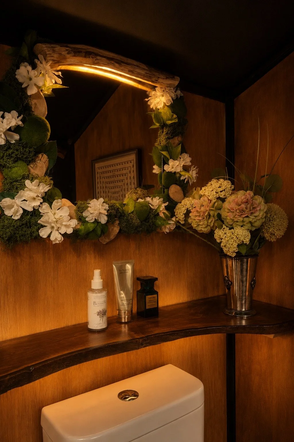 Illuminated floral mirror and live-edge timber shelf inside the outhouse, styled with flowers and small objects.