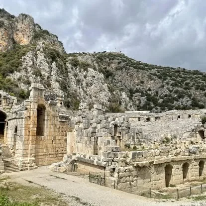 Ancient stone ruins with arches against a mountain backdrop under cloudy sky.