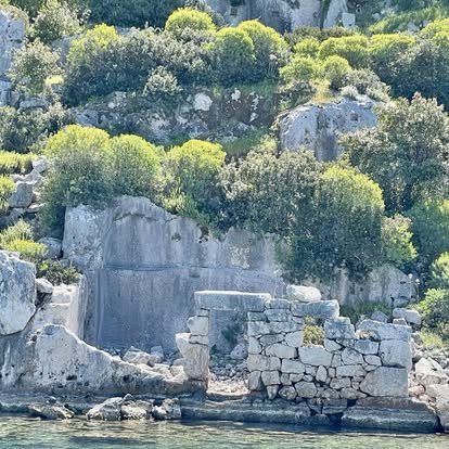 Cliffside with green bushes and stones along a water shoreline.