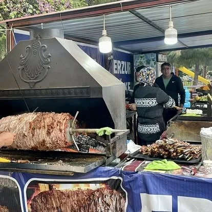 A large rotating spit of roasted meat at a stall, with two people preparing food behind the counter.