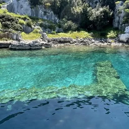 Clear turquoise water with submerged stairs leading into the water, surrounded by rocky and green landscape.