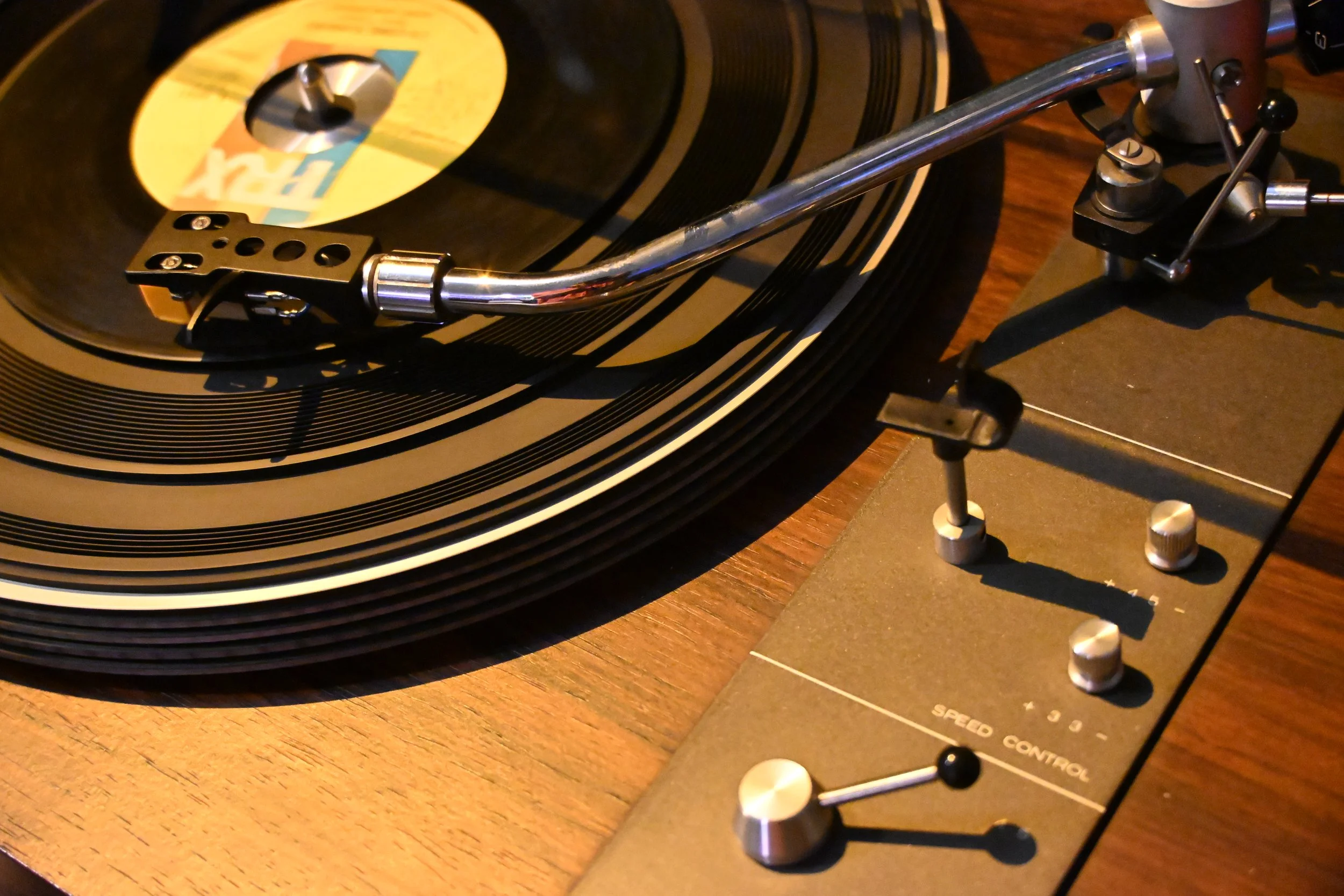 Close-up of a vinyl record on a turntable, with a tonearm ready to play, on a wooden surface.