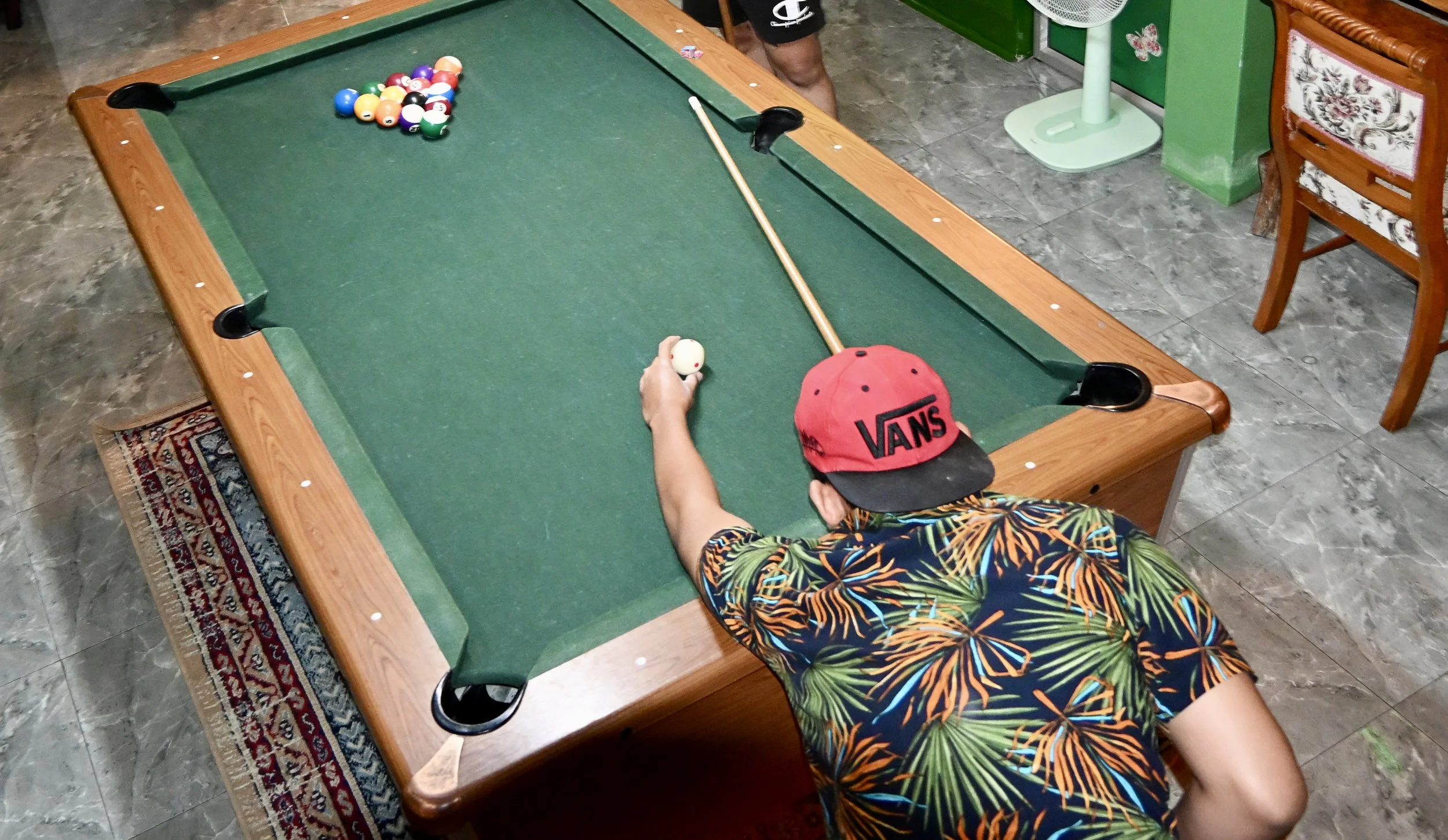Top-down view of a customer playing a game of pool on a green felt table at a cannabis-friendly social hub for travelers.