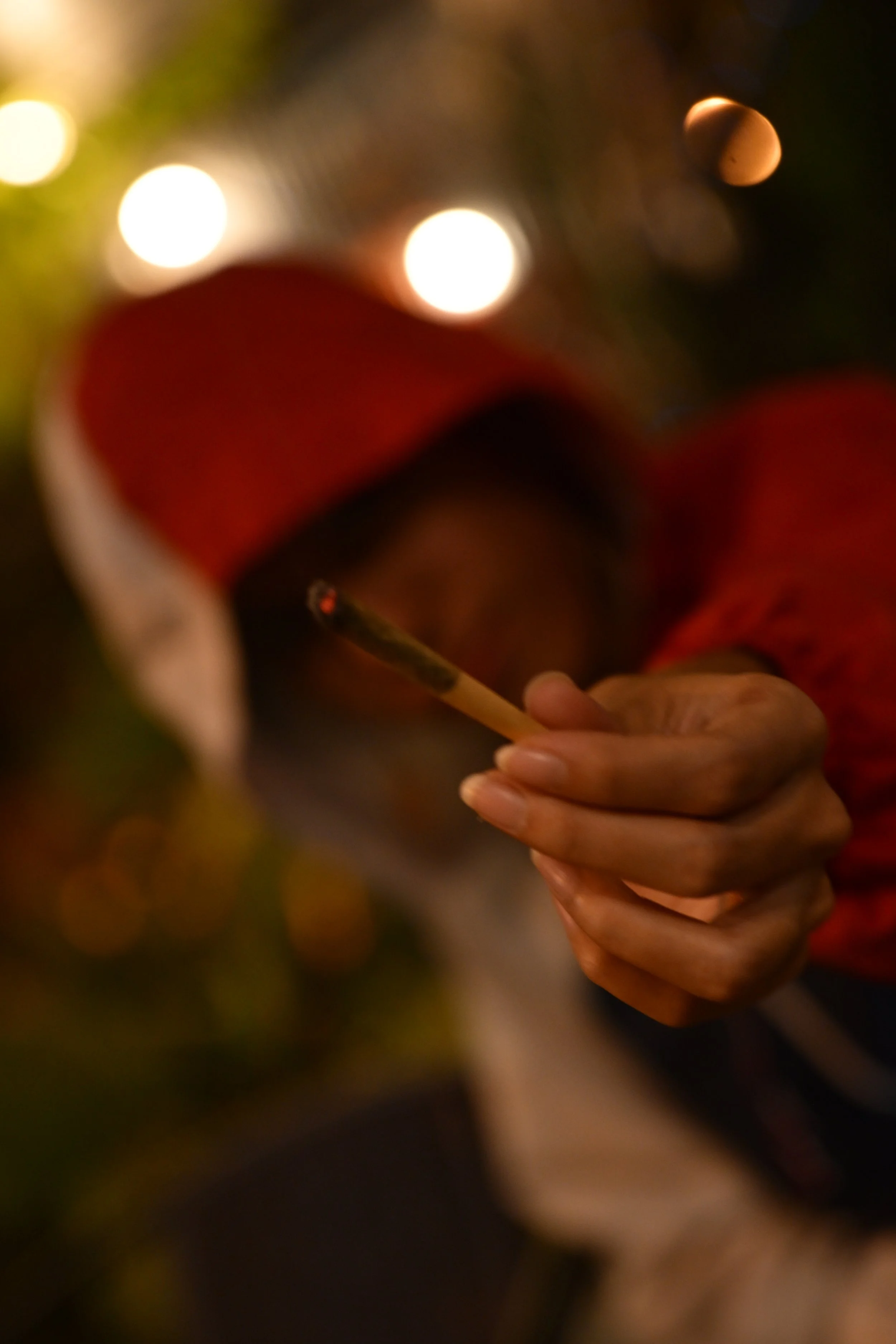 Close-up of a person holding a matchstick with a red and black head, in front of blurred colorful lights.