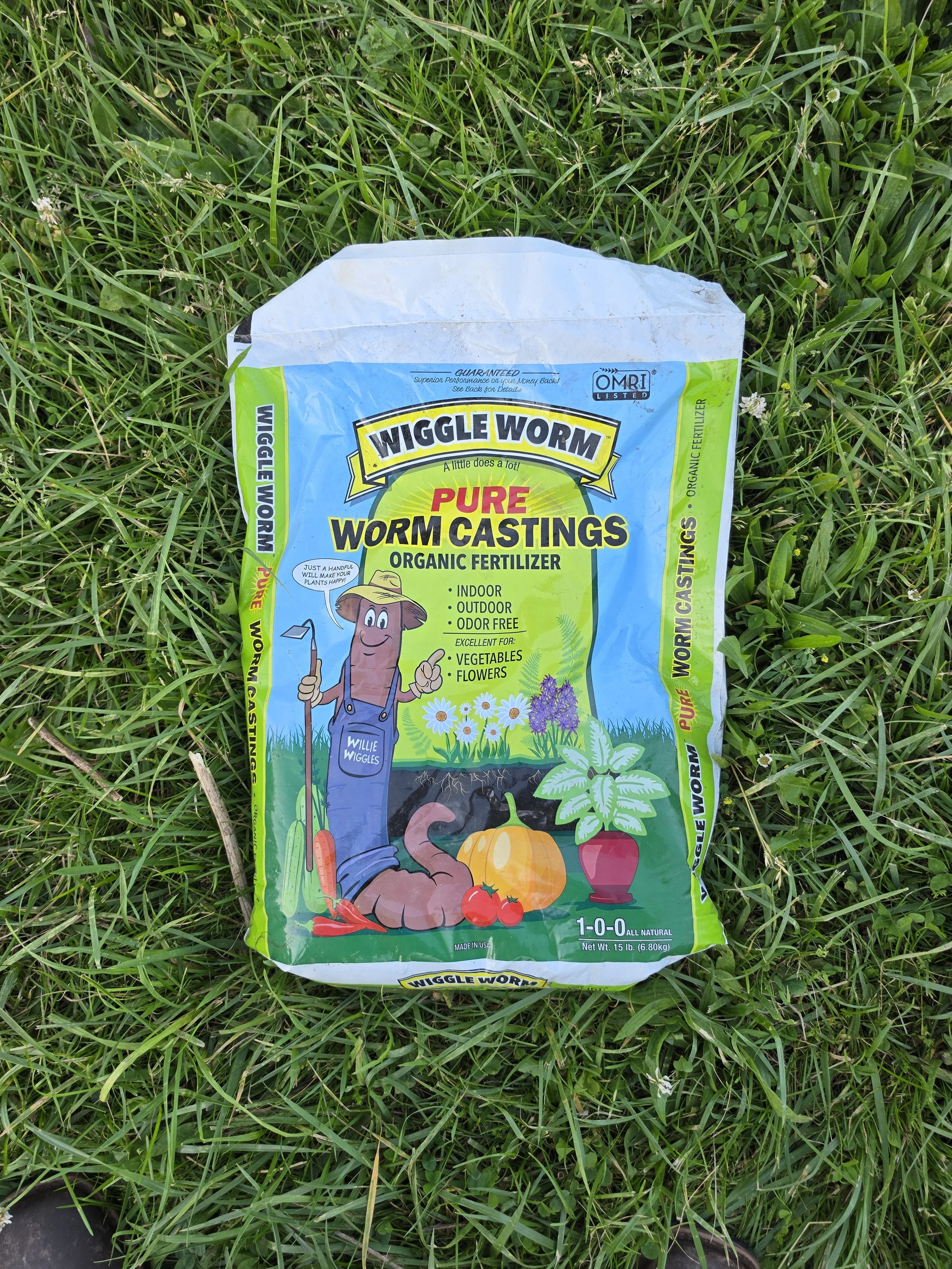 A bag of Wiggle Worm organic worm castings fertilizer resting on green grass.