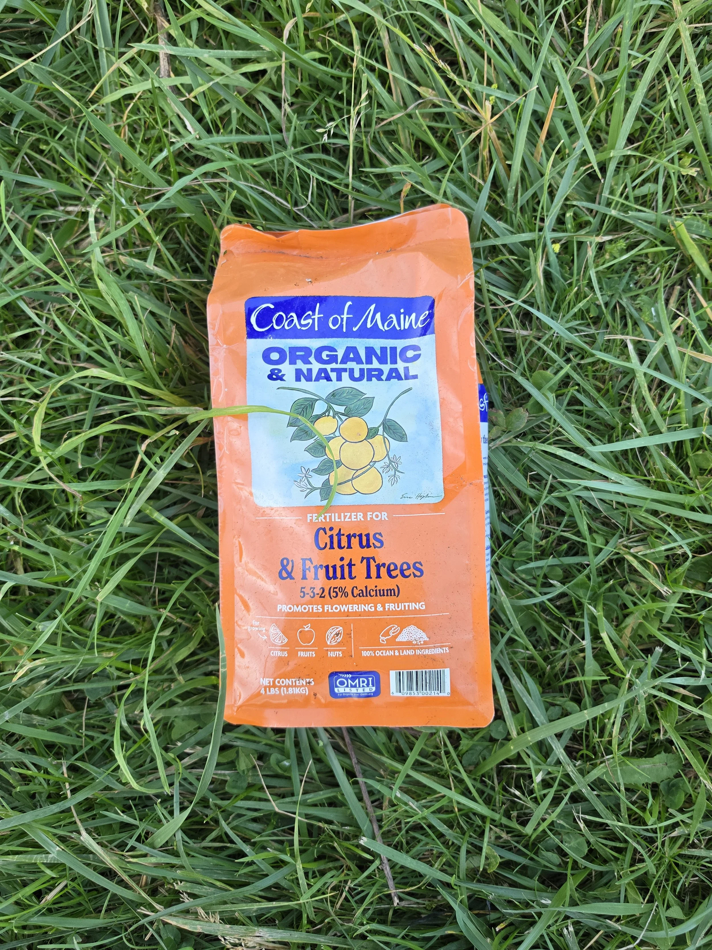 Packaging of fertilizer labeled 'Coast of Maine Organic & Natural' for citrus, fruit, and nut trees, lying on grass.