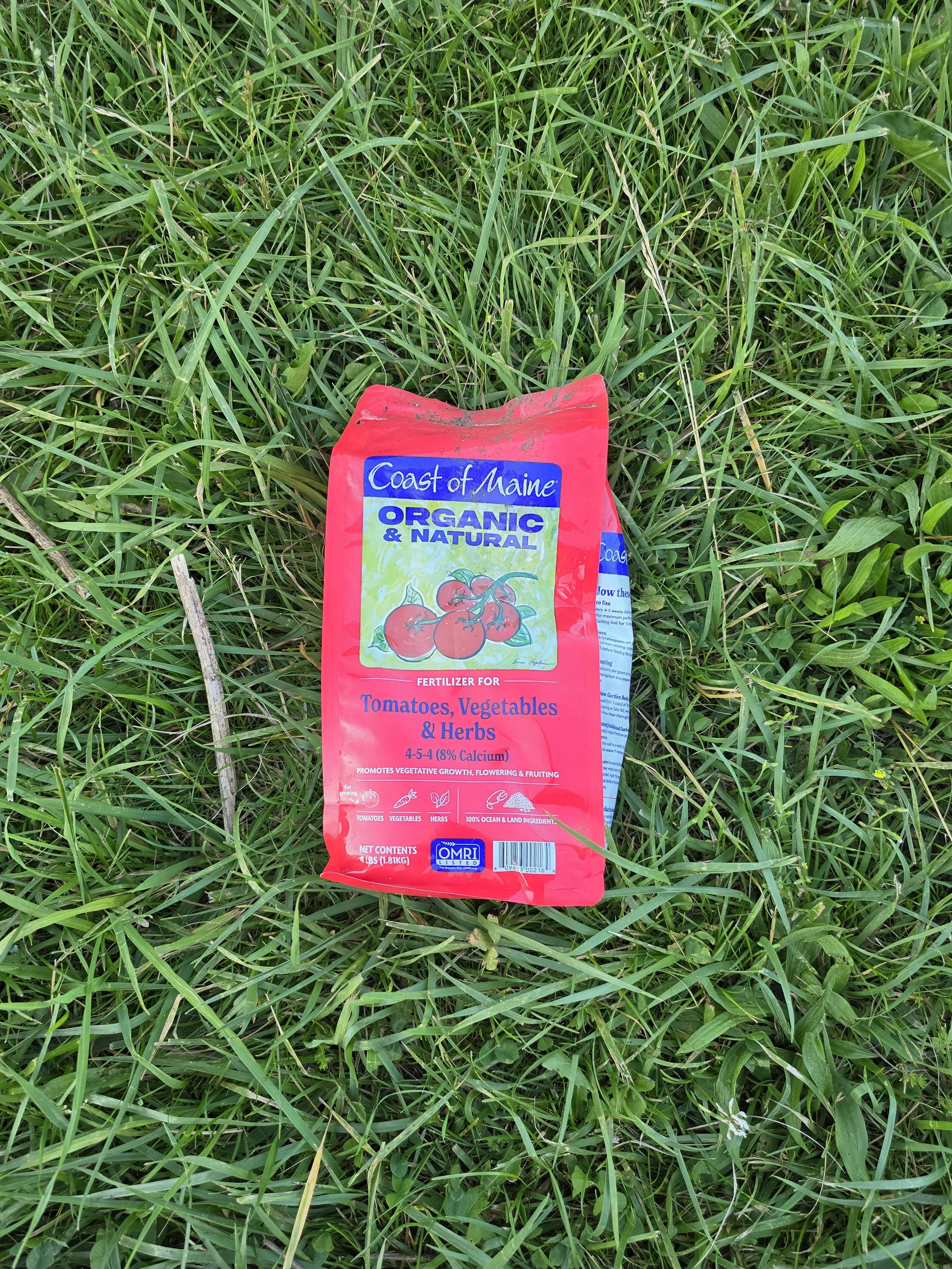 A bag of organic tomato, vegetable, and herb fertilizer lying in green grass.
