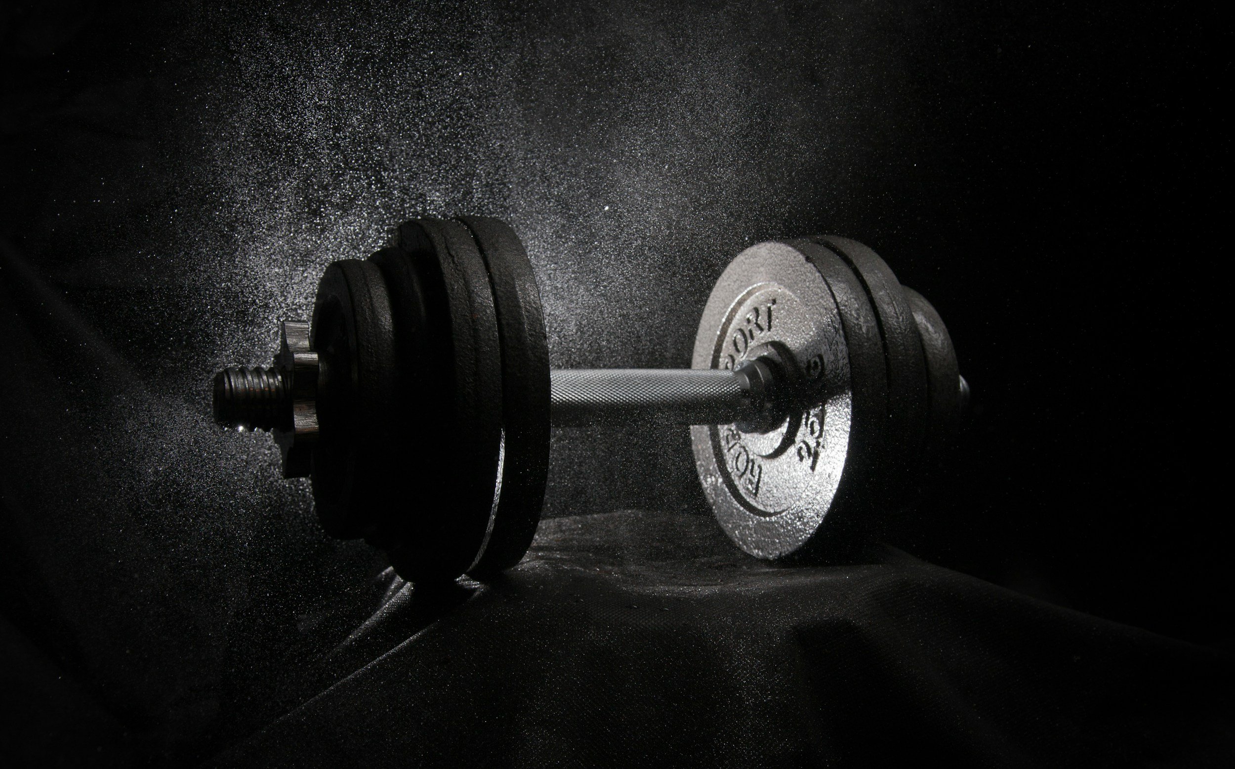 Black dumbbell with weight plates on a dark, textured surface with scattered chalk dust.