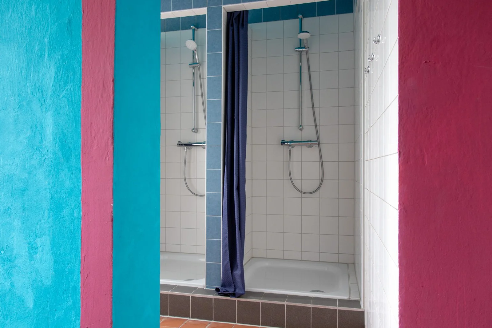 Doppel-Duschkabinen mit blaue Wände, beige Fliesen und bunter Wand im Vordergrund.