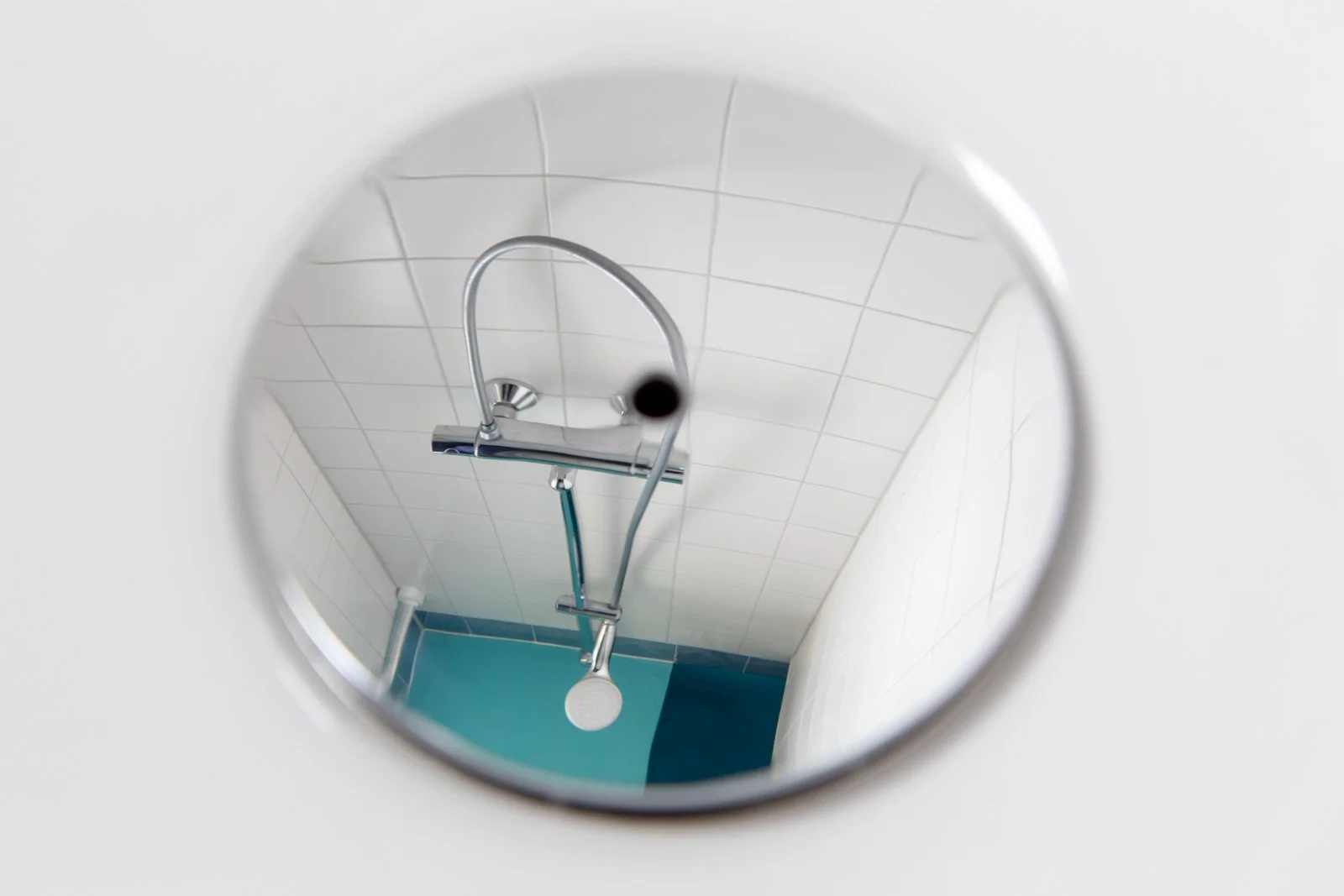 Rundspiegel zeigt Dusche mit Armatur, Duschkopf und weißer Wand im Bad.