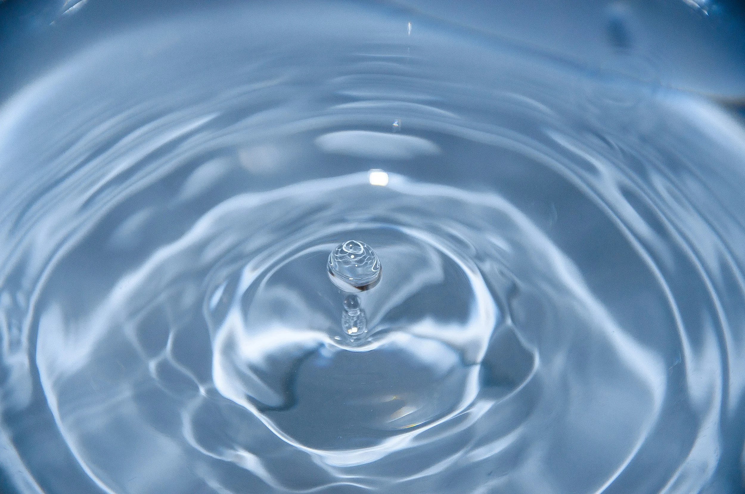 A close-up photograph of clear water with a small drop creating ripples on the surface.
