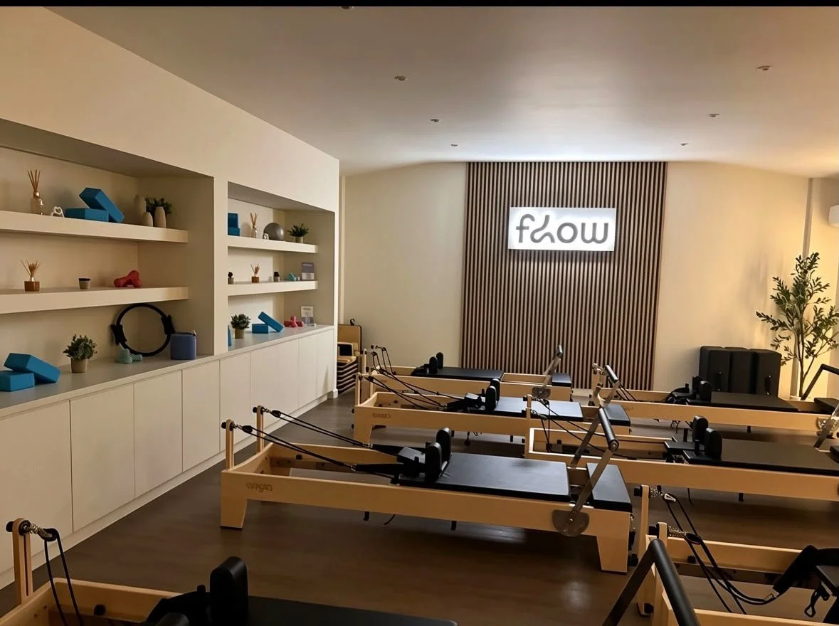 Pilates or fitness studio with reformer equipment, wooden wall panel, and decorative shelves with plants and accessories.