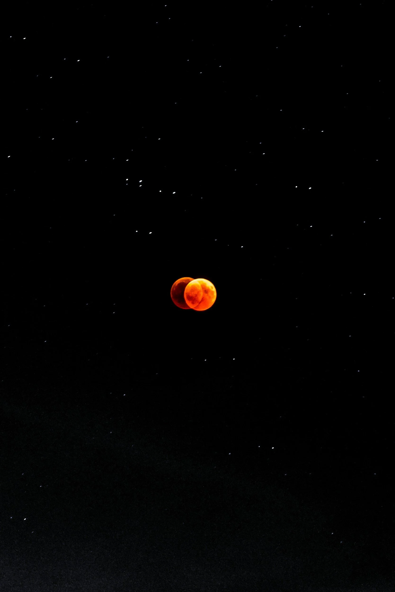 A lunar eclipse showing a blood moon with a reddish hue, set against a background of stars in the night sky.