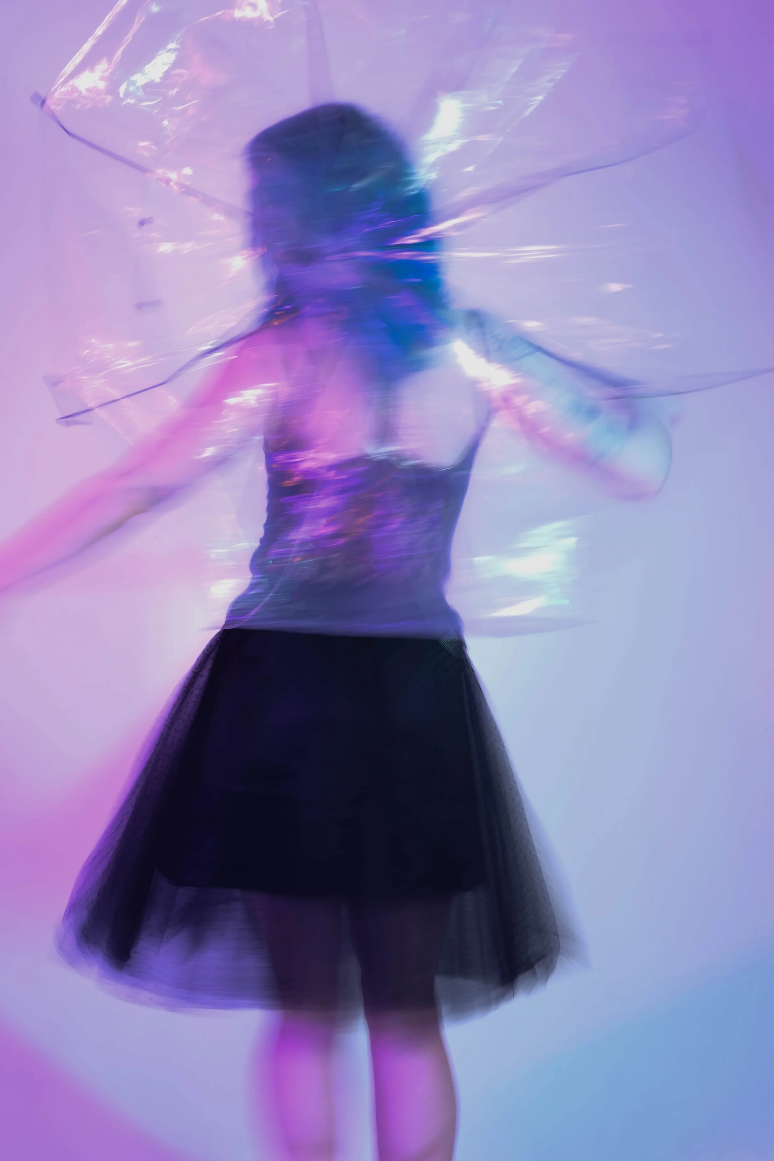 A person in a black dress holding a transparent umbrella with colorful lighting effects.