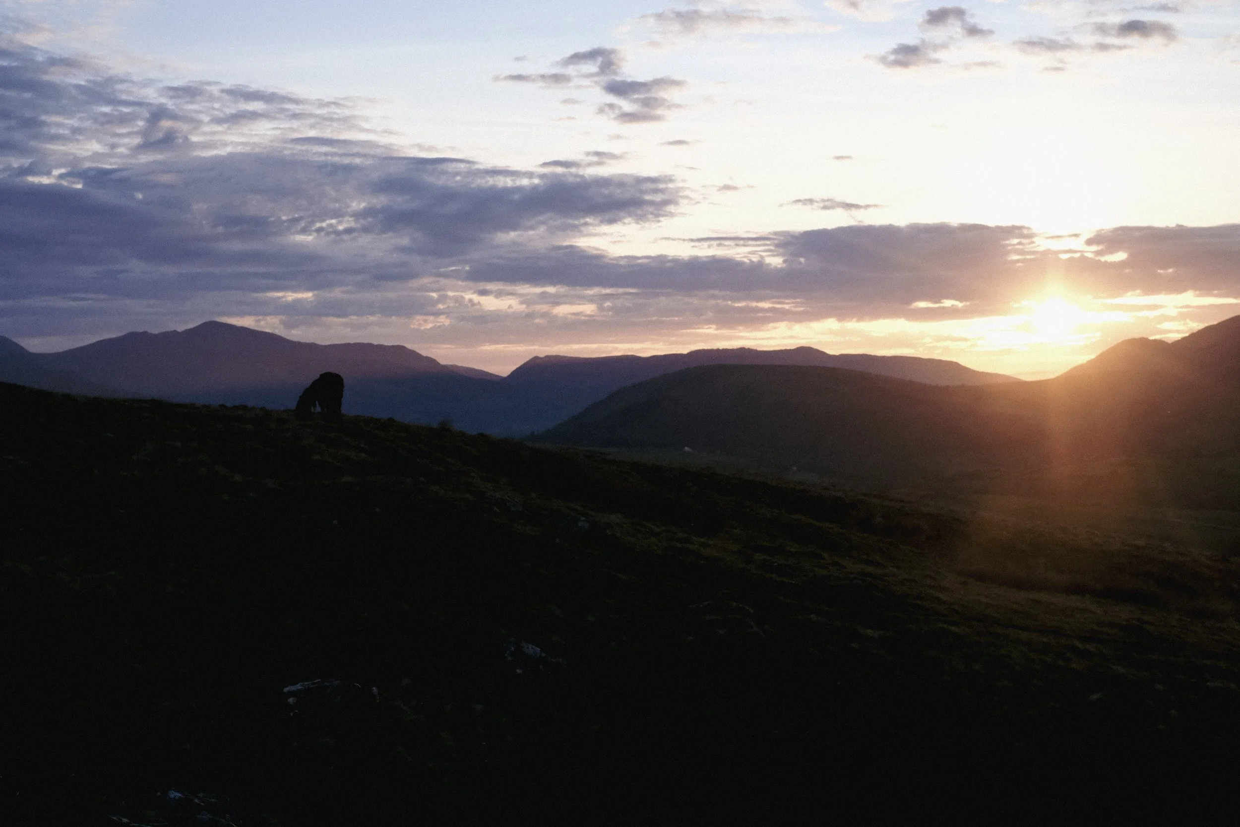 Sunset over a mountainous landscape with a silhouette of a rock formation in the foreground.