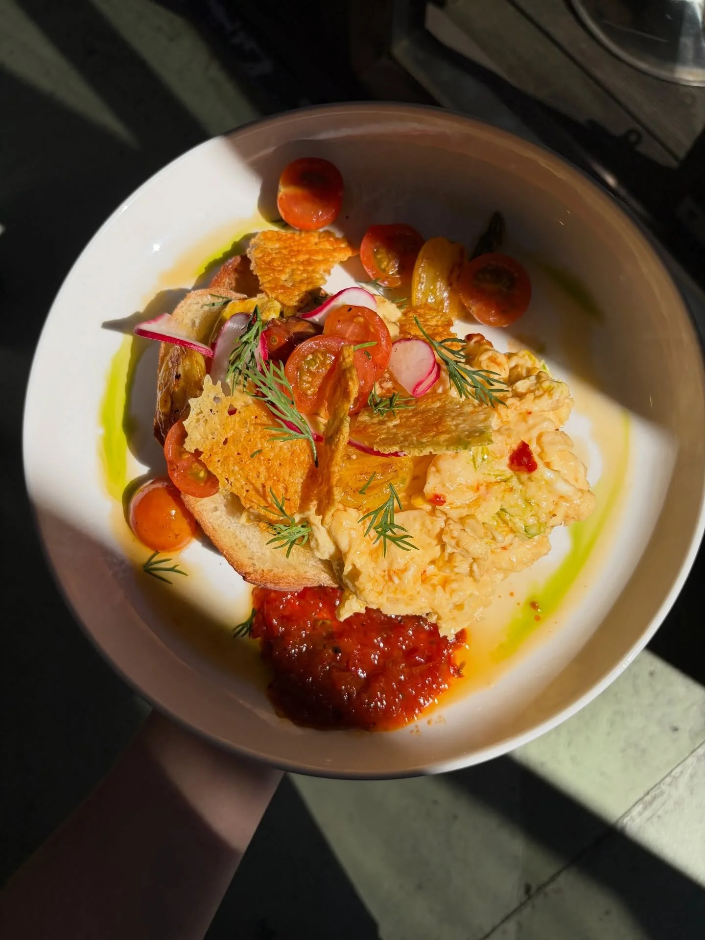Chilli scrambled eggs on toast with lightly pickled cherry tomatoes, garnished with herbs, herb oil, fresh chilli and parmesan crisps. 