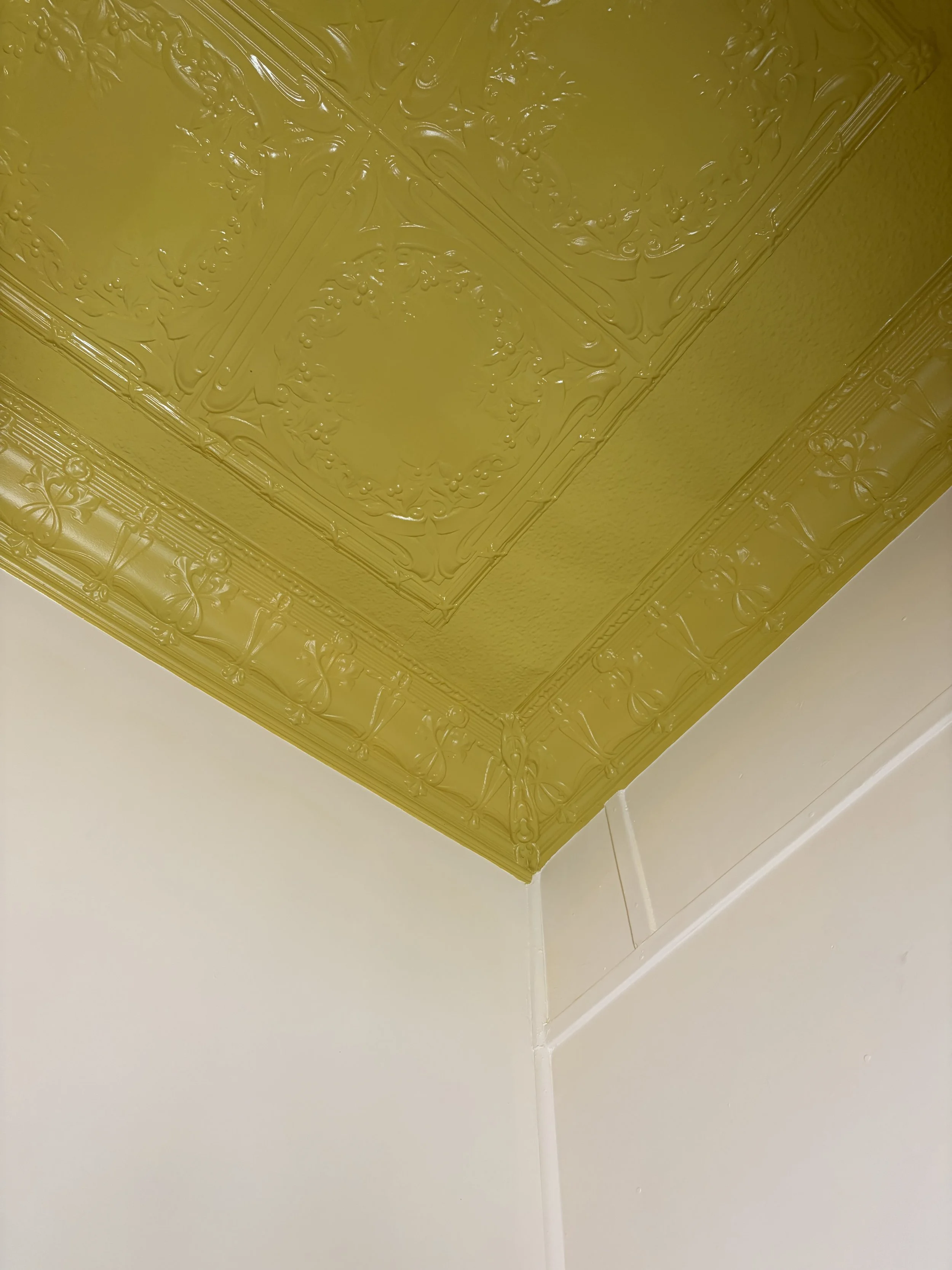 Ceiling with ornate decorative molding painted gold, meeting white walls.