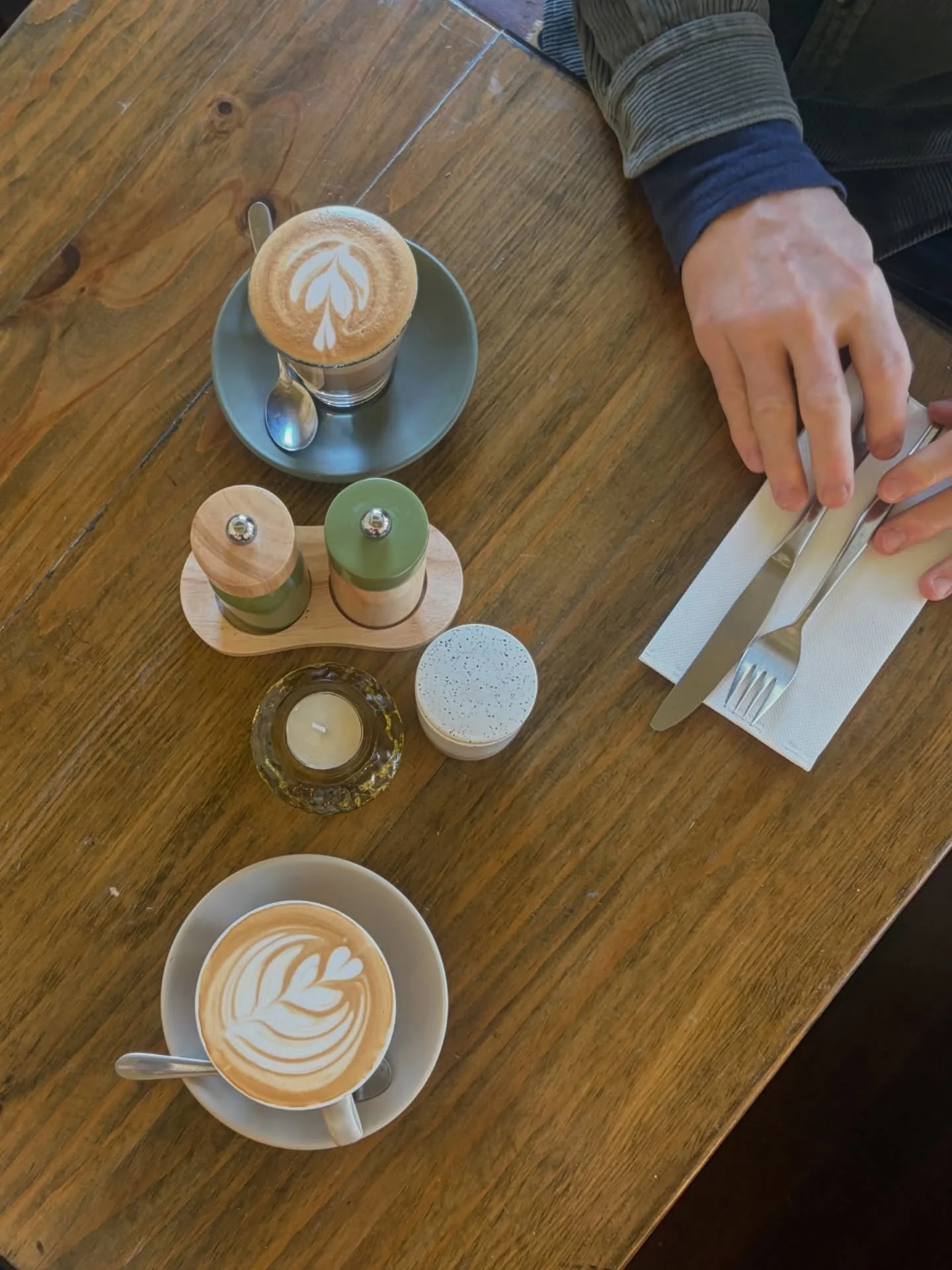 A wooden table with a Melbourne style latte art coffee, a cup of latte with a spoon, and retro style green salt and pepper shakers.