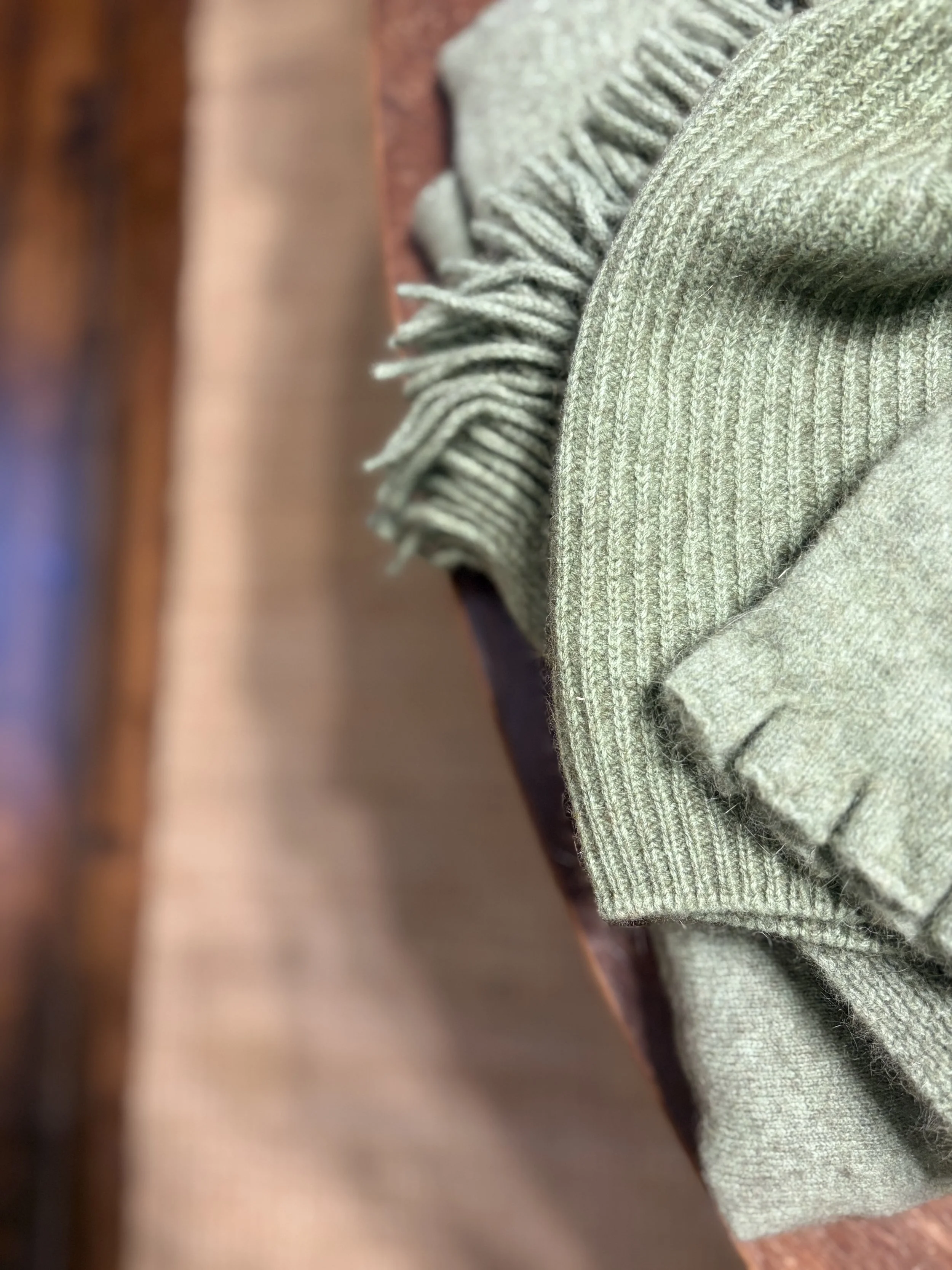Close-up of green knitted scarf, wrap, gloves and fingerless gloves, with a textured pattern and ribbed cuff, draped over a vintage table. Knitwear is sheeps wool and possum wool.