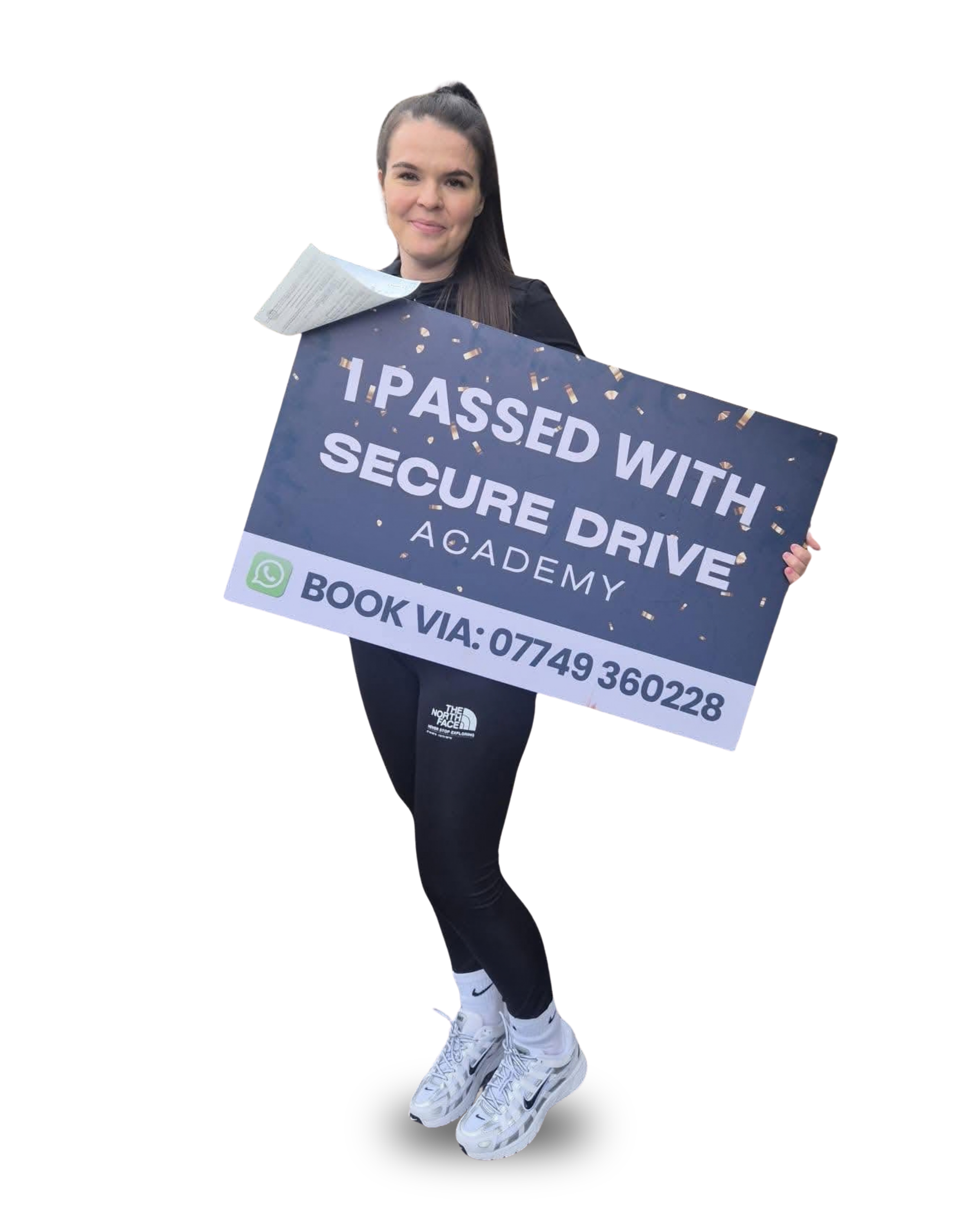 A young woman holding a sign that says 'I PASSED WITH SECURE DRIVE' in front of her body, smiling with a confident expression, wearing white athletic shoes, black leggings, and a black jacket, with a black background.