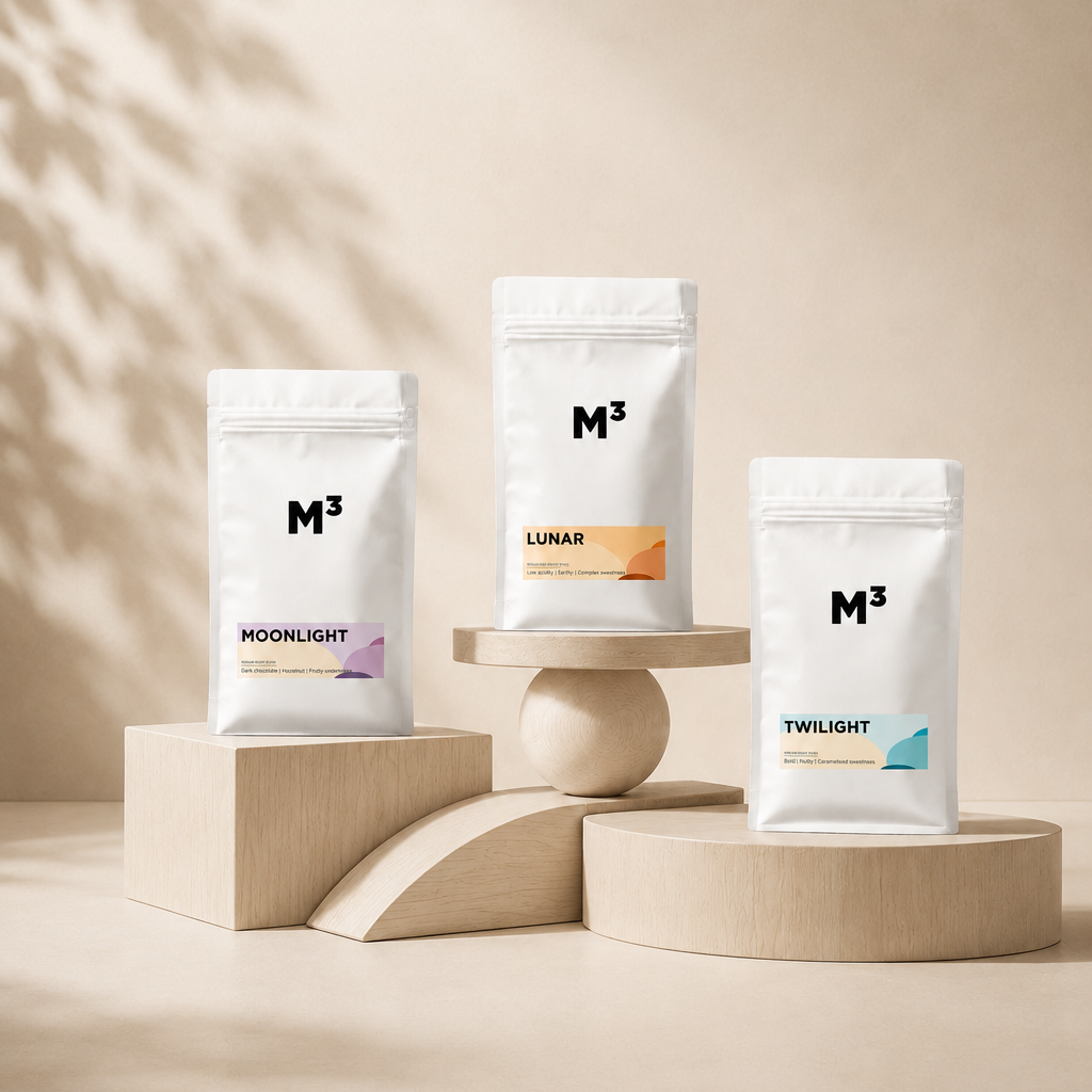 Three white packages of M³ tea with colorful labels for Moonlight, Lunar, and Twilight, displayed on wooden platforms against a beige background.