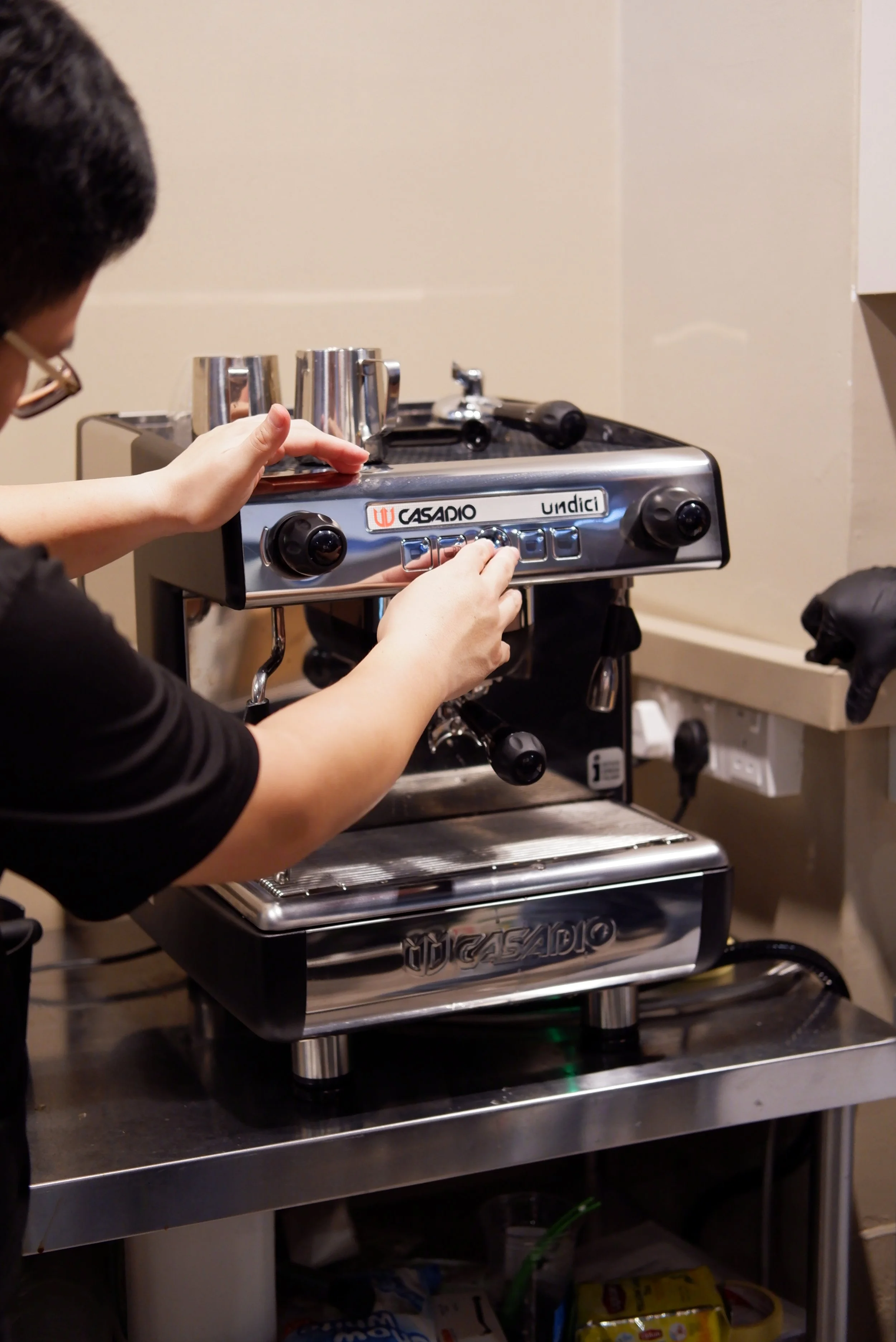 A person adjusting settings on a stainless steel espresso machine in a kitchen or coffee shop.