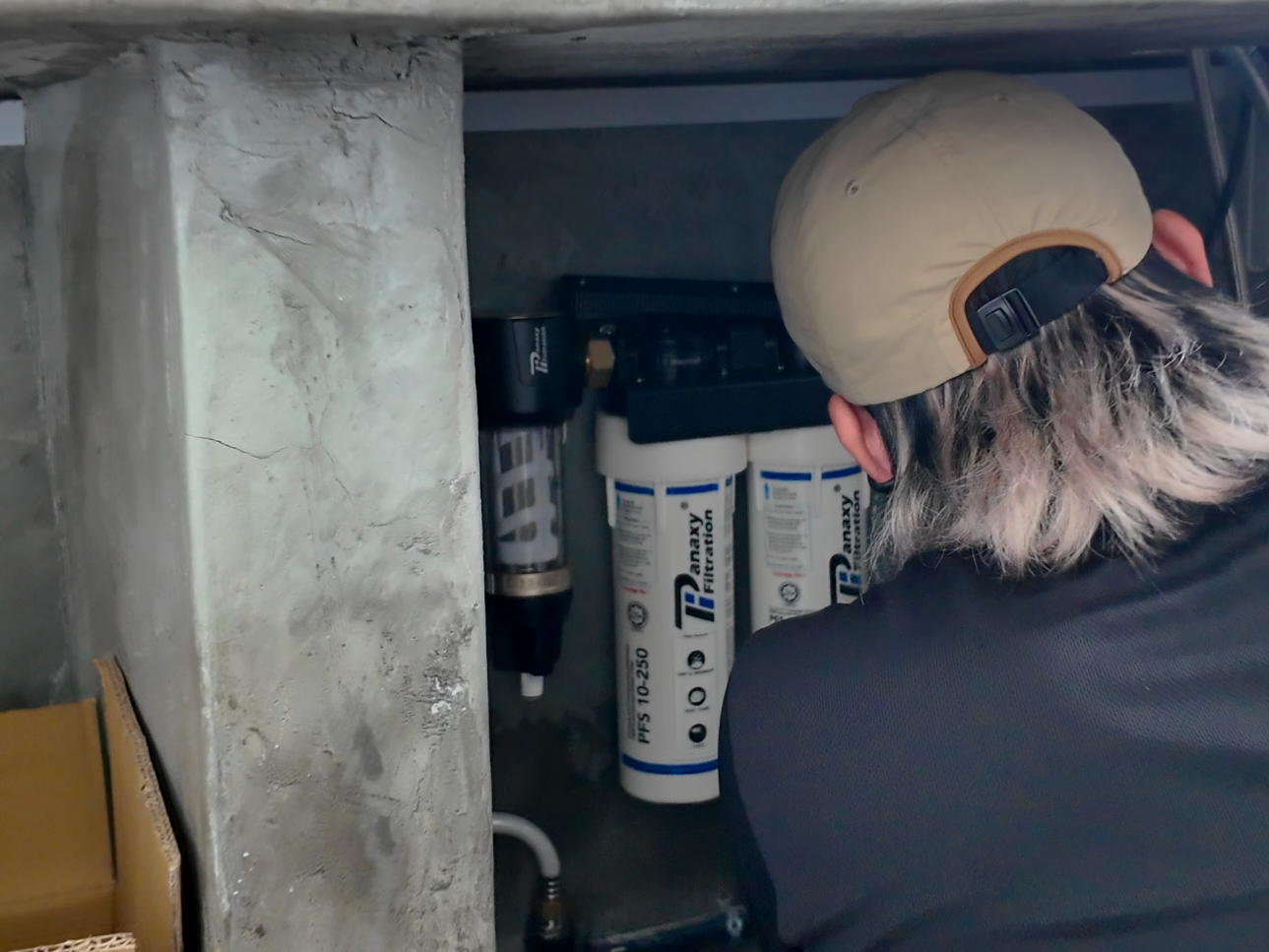 Person installing or inspecting a water filtration system under a kitchen or utility sink, with filters labeled 'Parax' and settings 'PFS 10-250'.