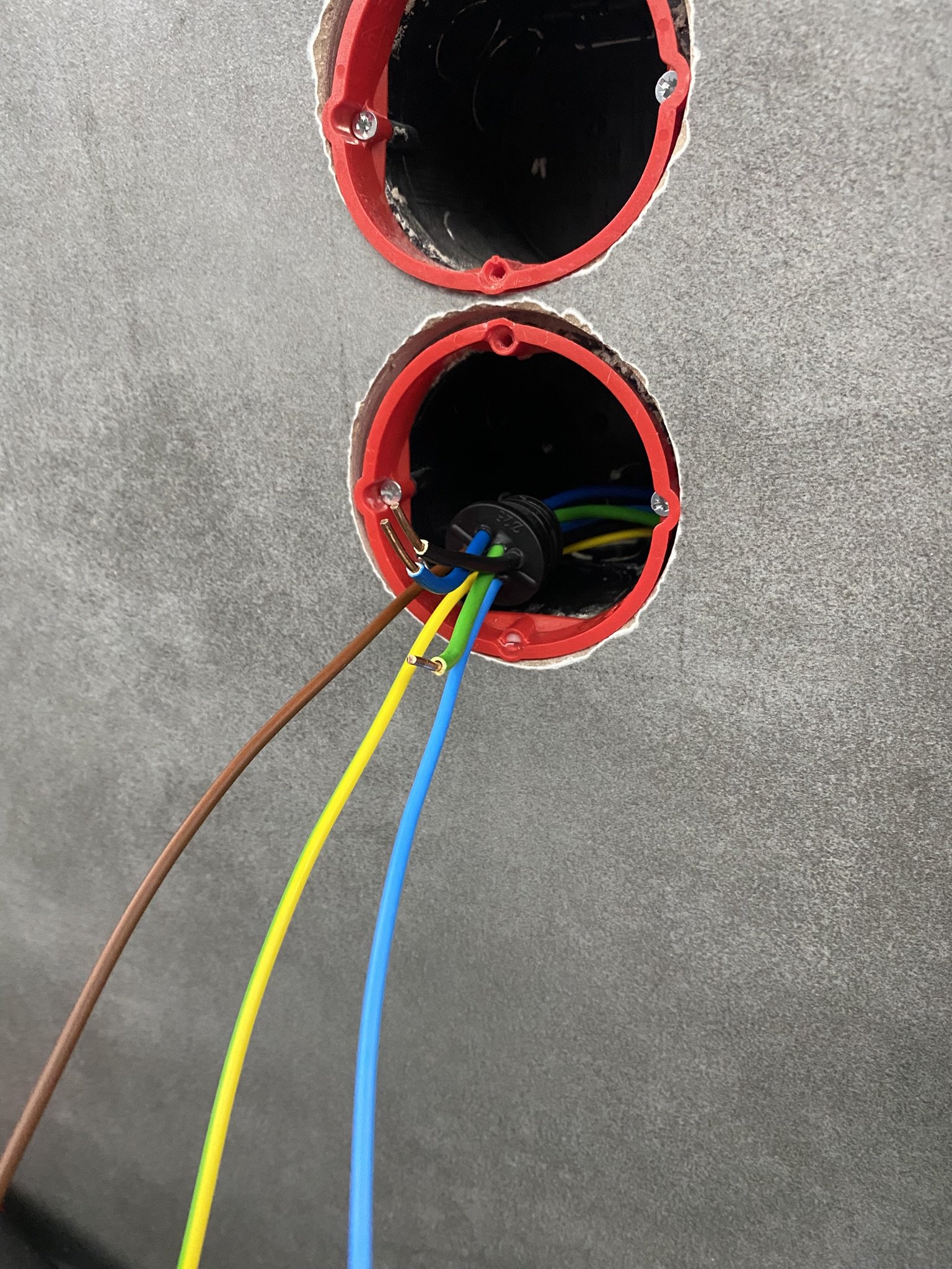 Építés vagy felújítás alatti fal részlete, amelyben szakszerűen falba süllyesztett elektromos vezetékek, két piros, kerek szerelvénydoboz és légtömör dugó látható, utóbbi, a hőhídmentesség miatt.