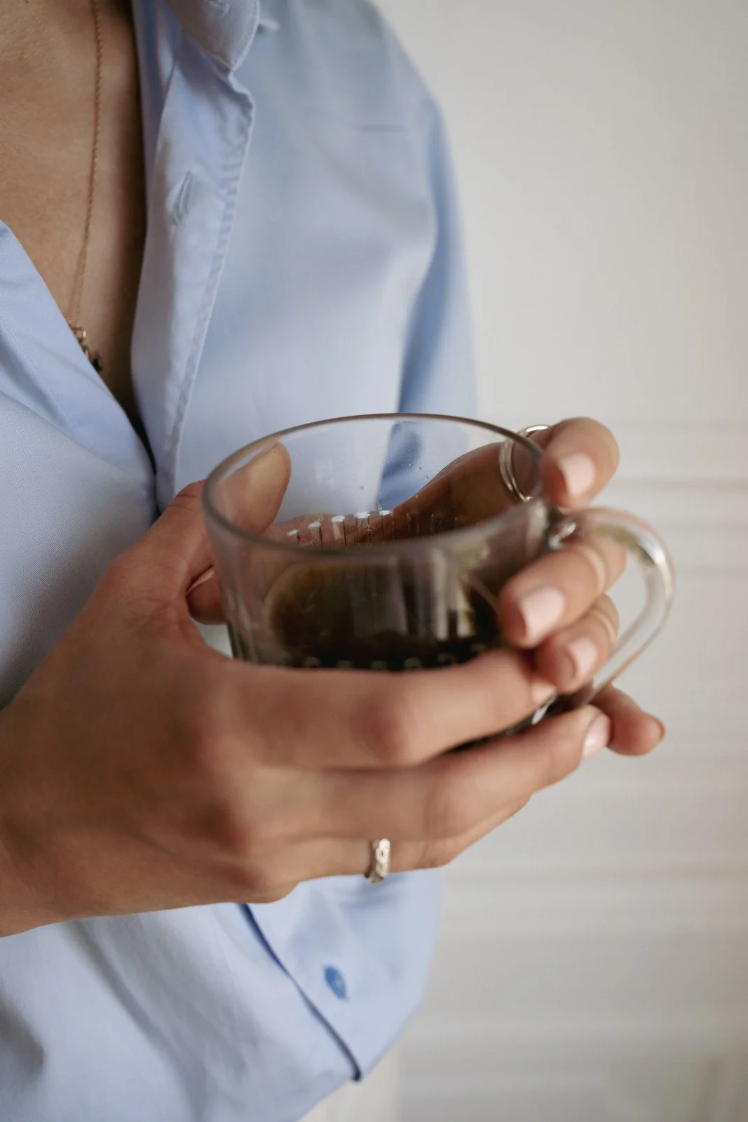 Person wearing a light blue shirt holding a glass mug of coffee.