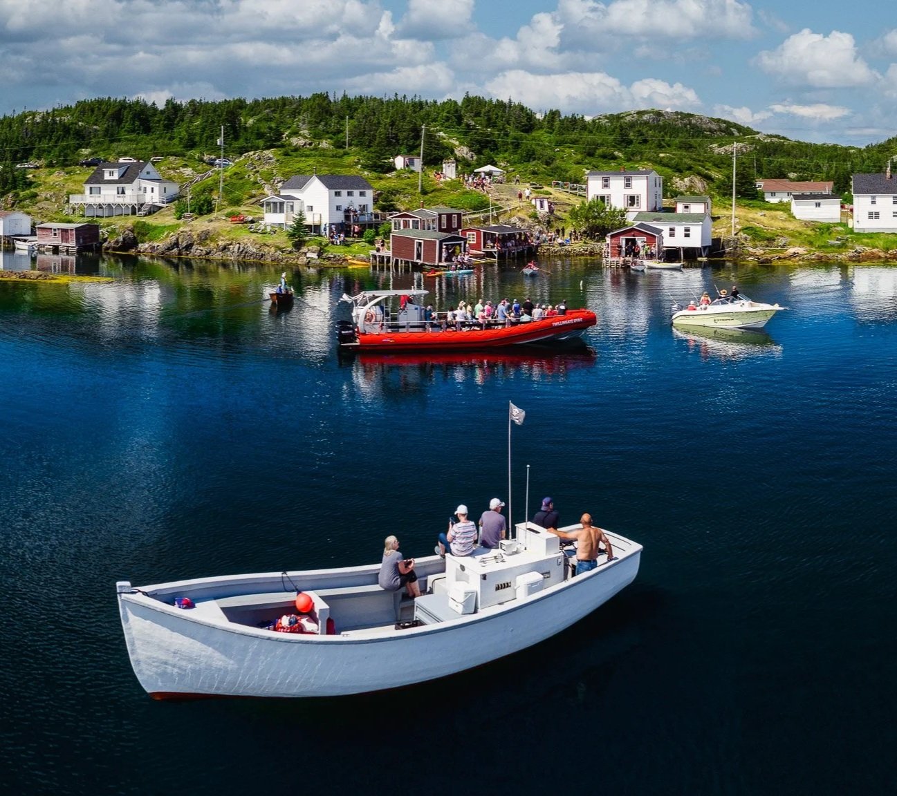 Boats on calm water near coastal houses with people on shore in a scenic, rural seaside village.