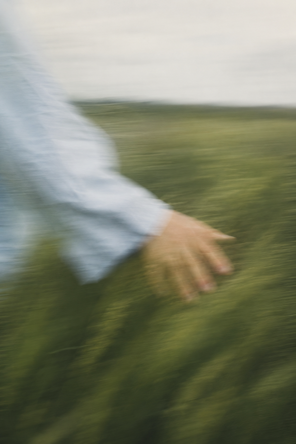 Blurred image of a person in a white shirt reaching out with their hand, with a green grassy background.