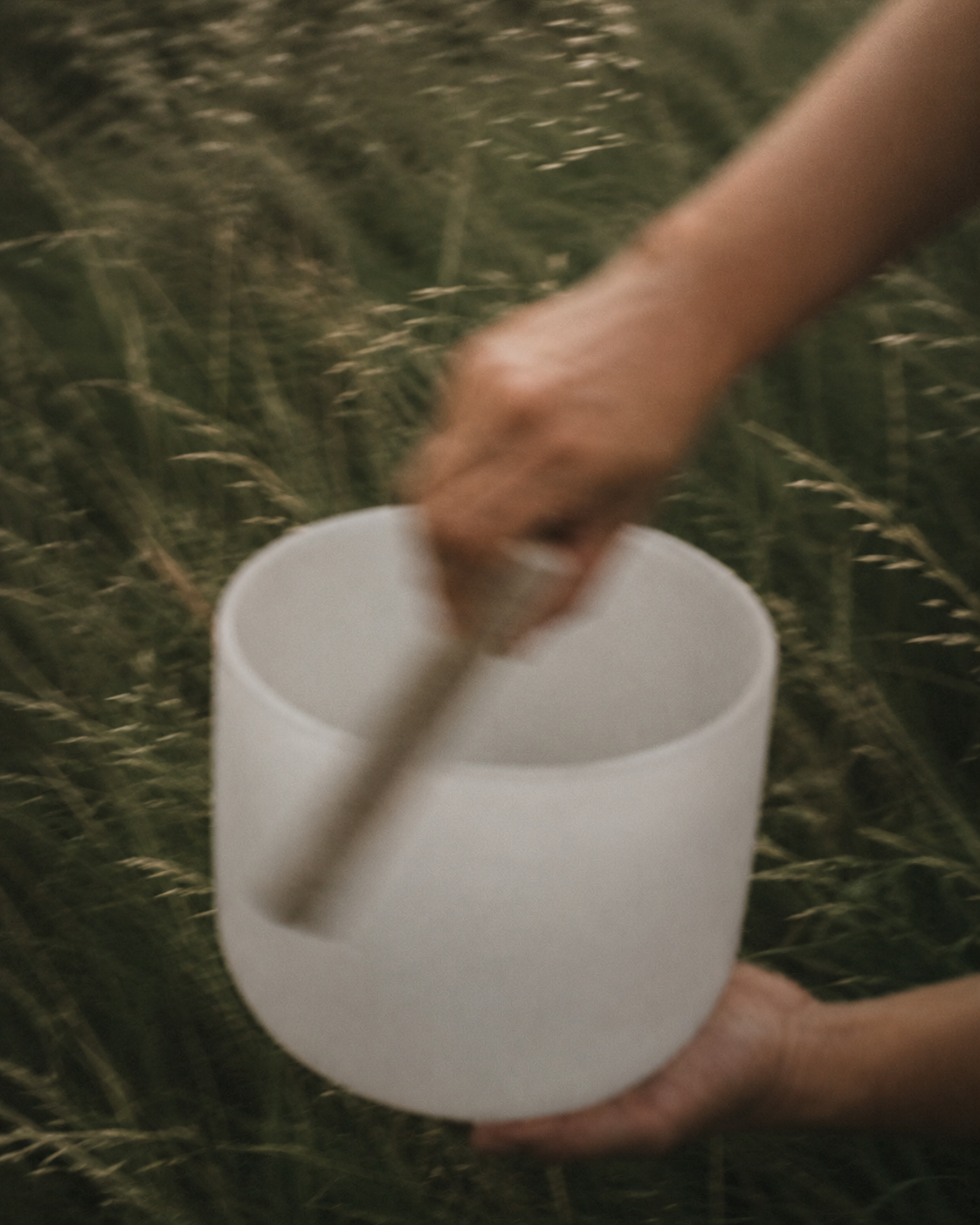 A person holding a white ceramic mug in a grassy outdoor setting.