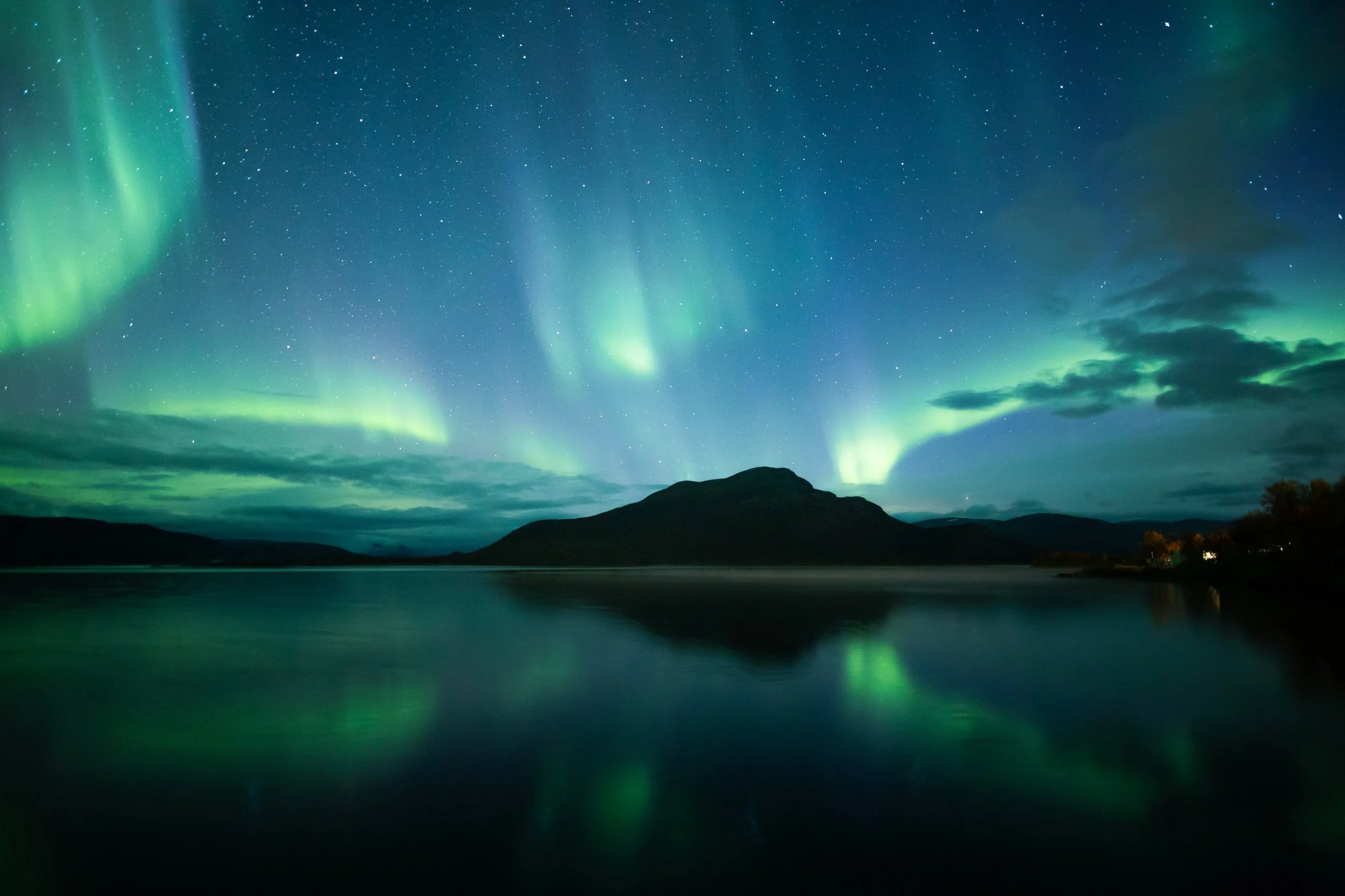 Northern lights (aurora borealis) glowing green in the night sky over a body of water and mountains.