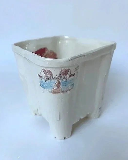 A white square ceramic container with a landscape scene painted on one side, featuring a dock, boats, and water.
