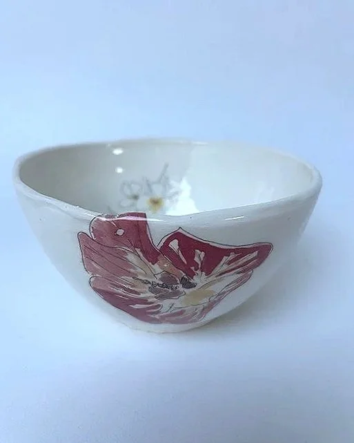 A small white ceramic bowl with a floral design on the side, partially filled with water, placed on a white surface against a light blue background.