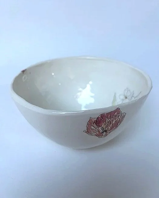 A white ceramic bowl with a floral design on its exterior, empty and with a reflective glaze inside.
